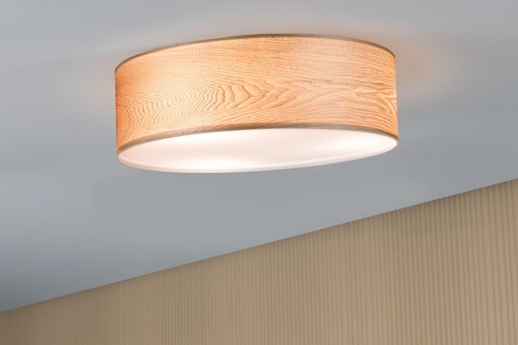 Owalna lampa sufitowa z fakturą słojów drewna i ciepłym oświetleniem.