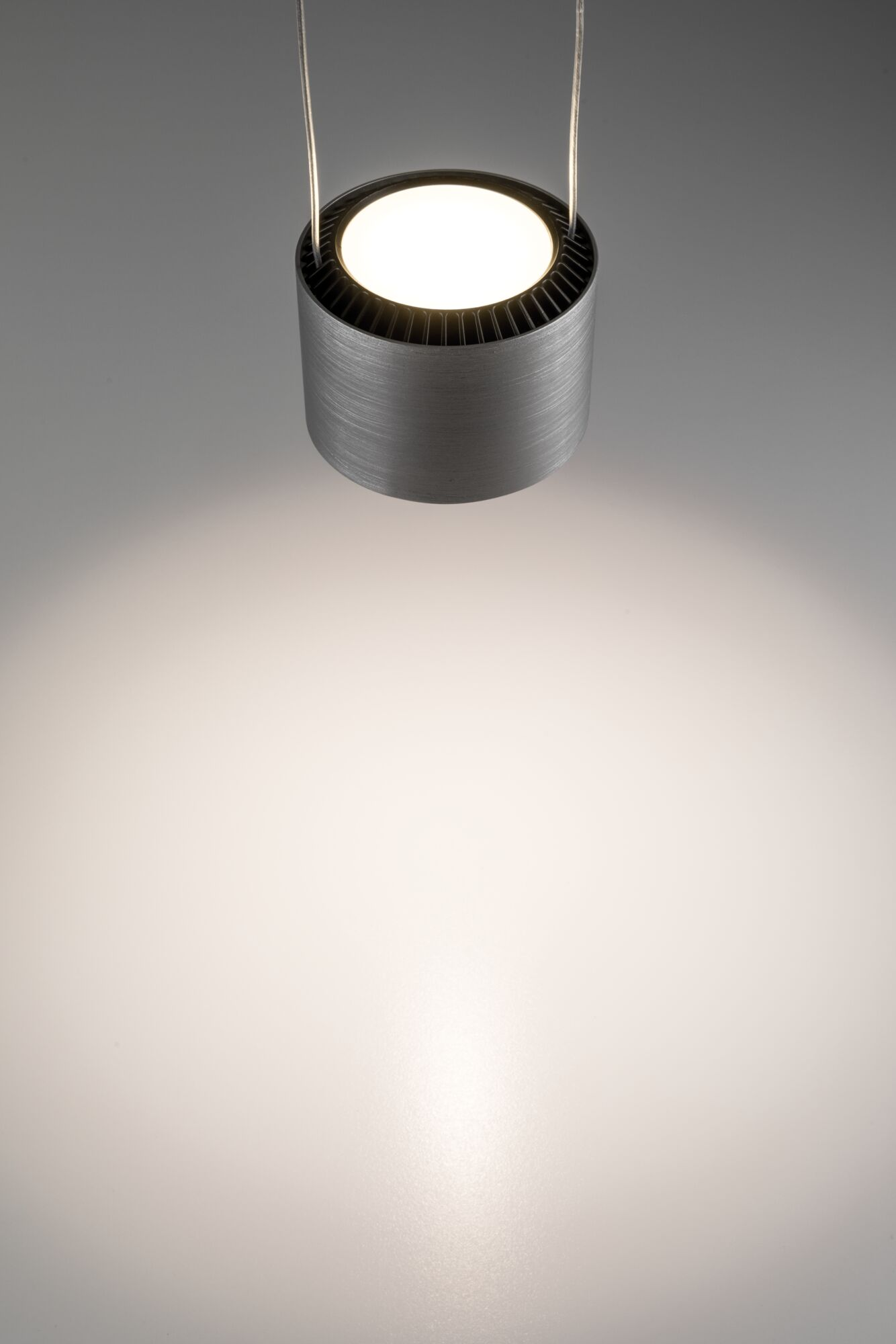 Zylindrische Pendelleuchte aus gebürstetem Metall leuchtet nach unten.