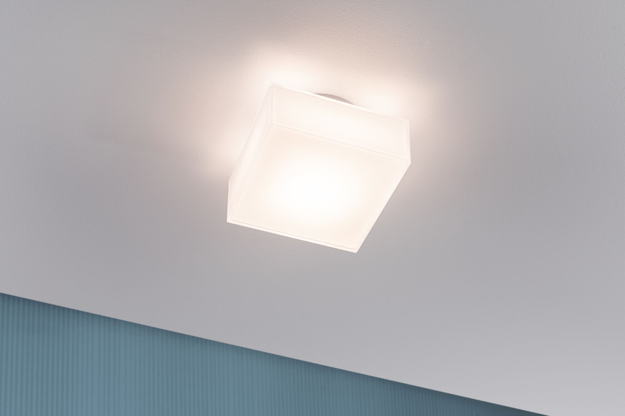 Ein rechteckiger Deckenstrahler mit mattweißem Gehäuse leuchtet auf einer weißen Decke.