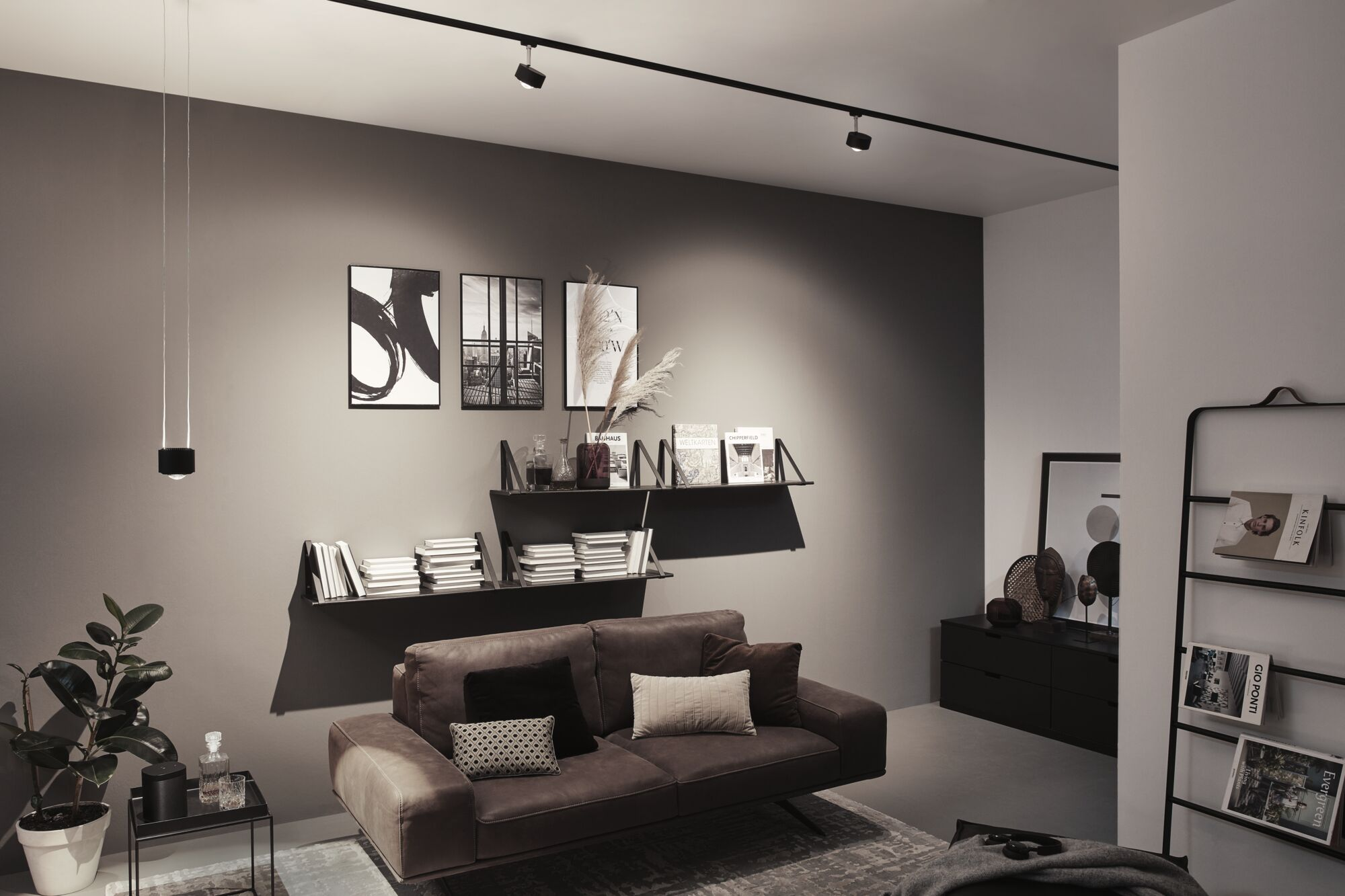 Modernes Wohnzimmer mit braunem Sofa, Bücherregalen, Kunst und Beleuchtung.