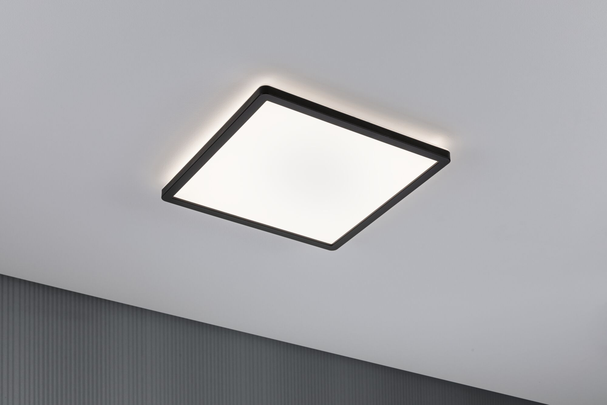 Ein moderner, quadratischer Deckenleuchter mit schwarzem Rahmen leuchtet an einer Decke.