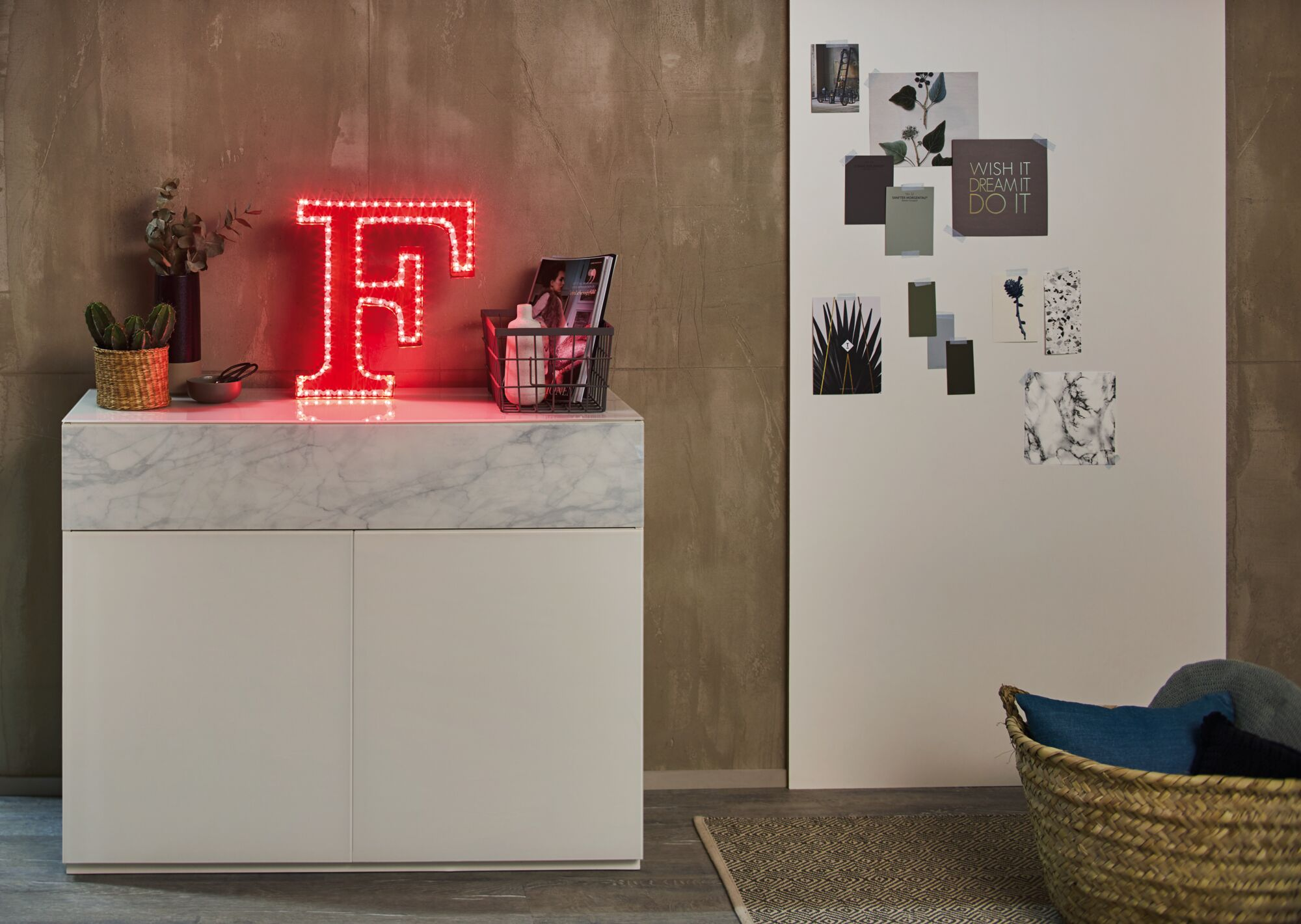 Ein rotes Neon-F auf einem Schrank mit Marmorplatte, daneben Pflanzen und ein Korb.