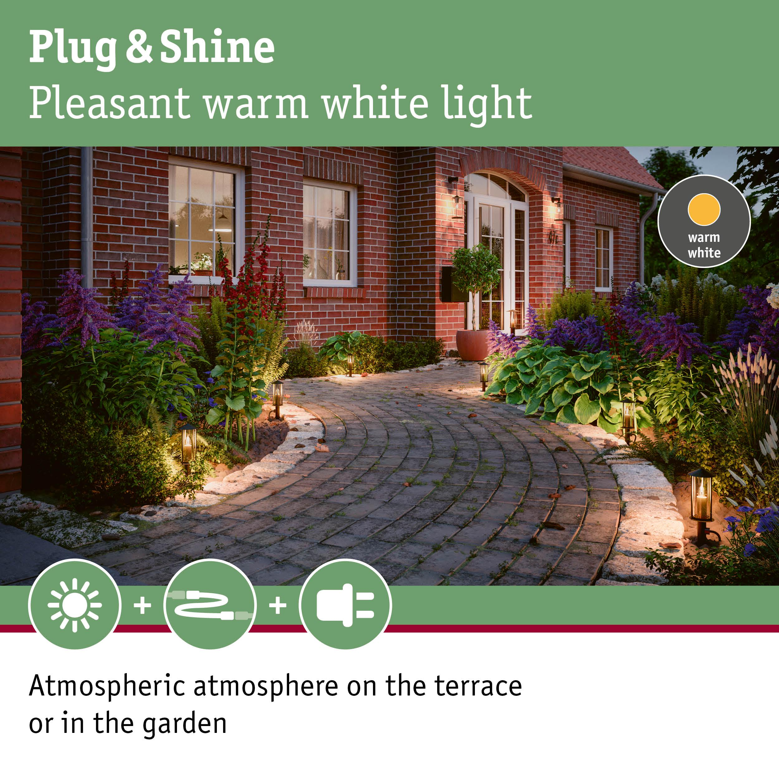 Ein Ziegelhaus mit Gartenbeleuchtung und einem gepflasterten Weg. Warmweiße Lichter.