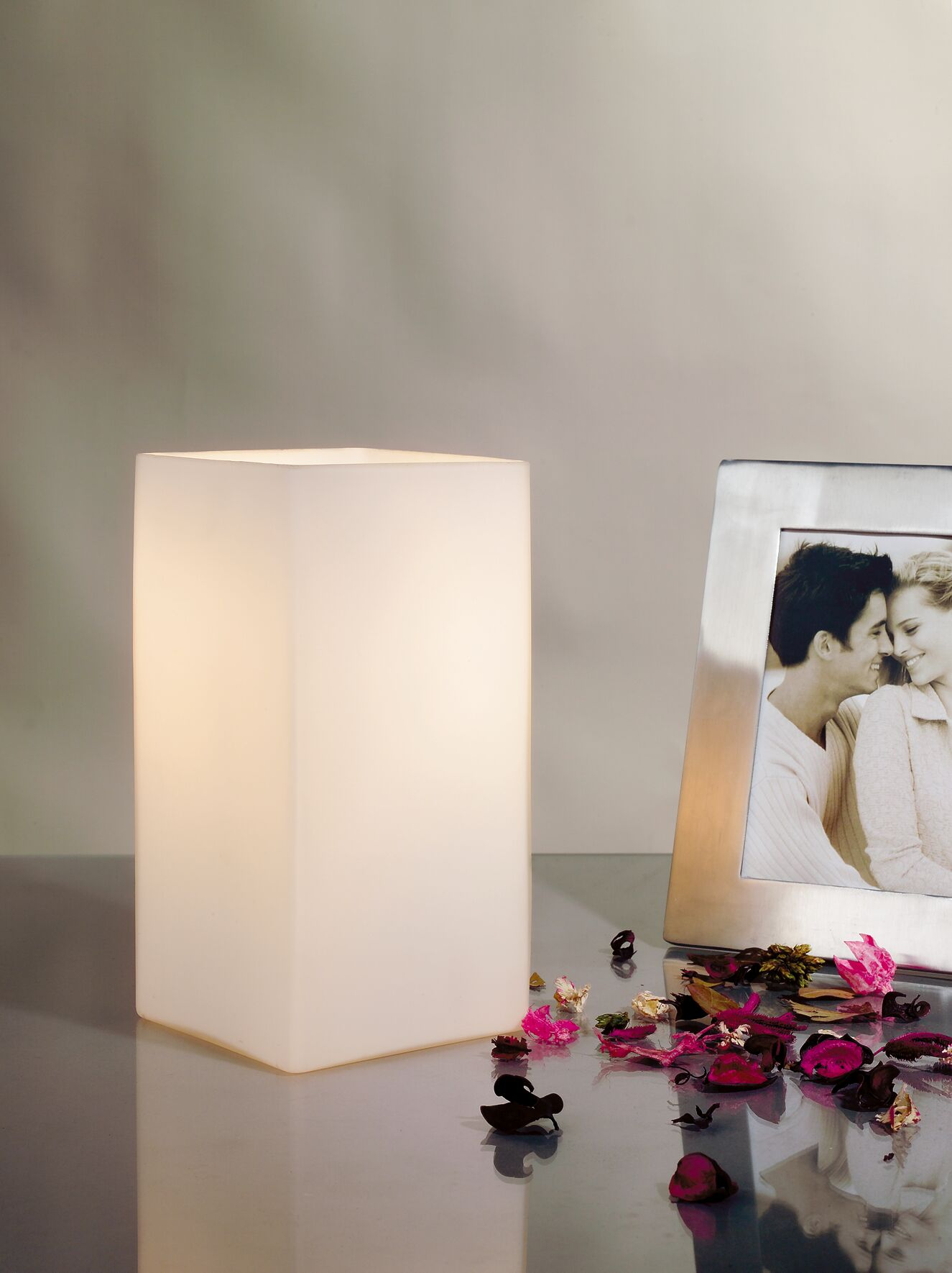 Świecący klosz lampy w kształcie sześcianu obok srebrnej ramki na zdjęcie z parą.