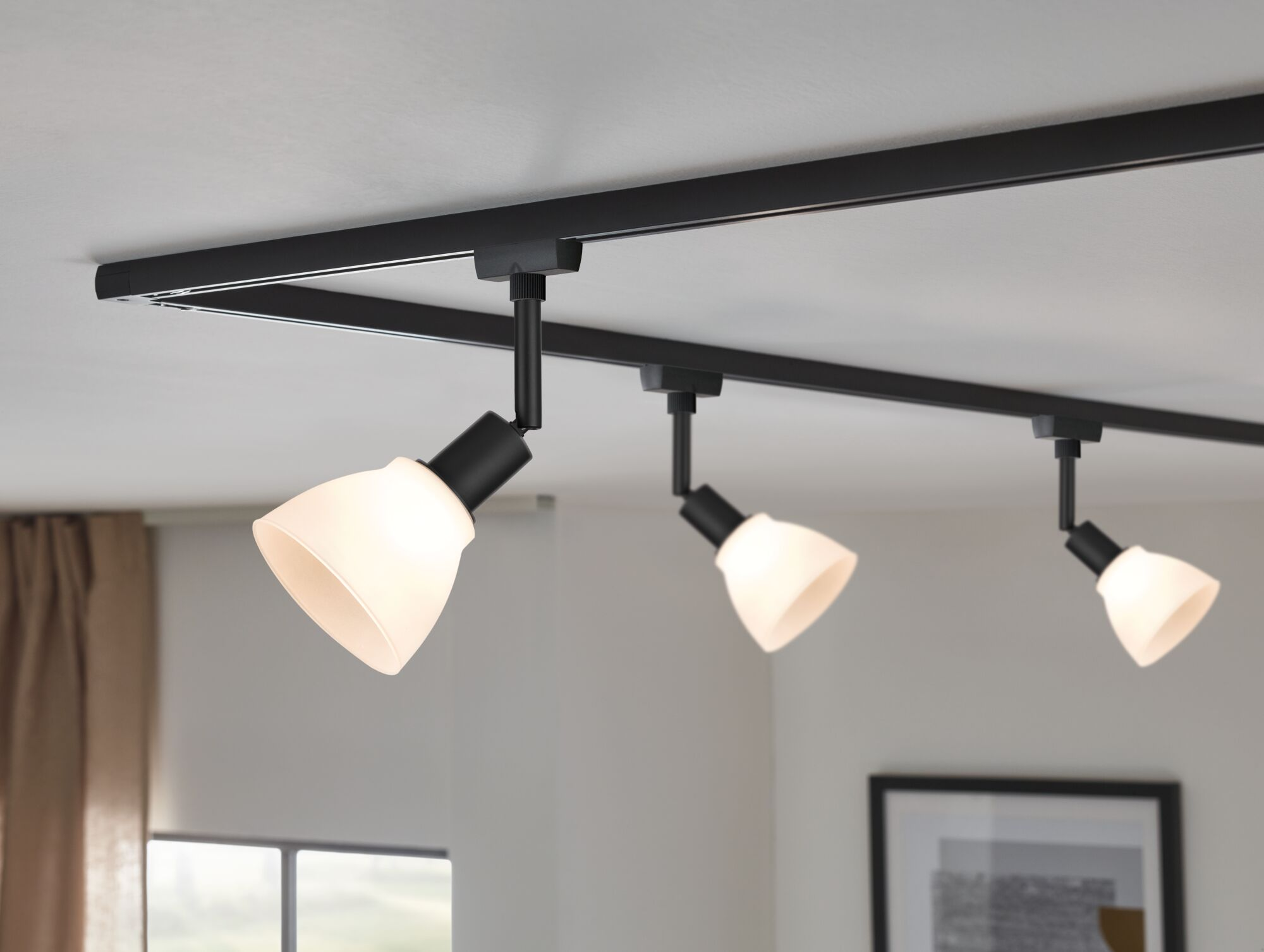 Eine schwarze Stromschienenleuchte mit drei Lampen mit weißen Schirmen an einer Decke.