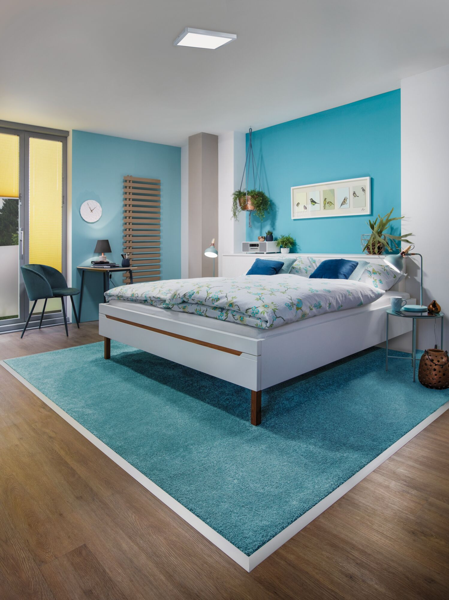 Una camera da letto con tappeto blu, letto bianco, scrivania e finestra.