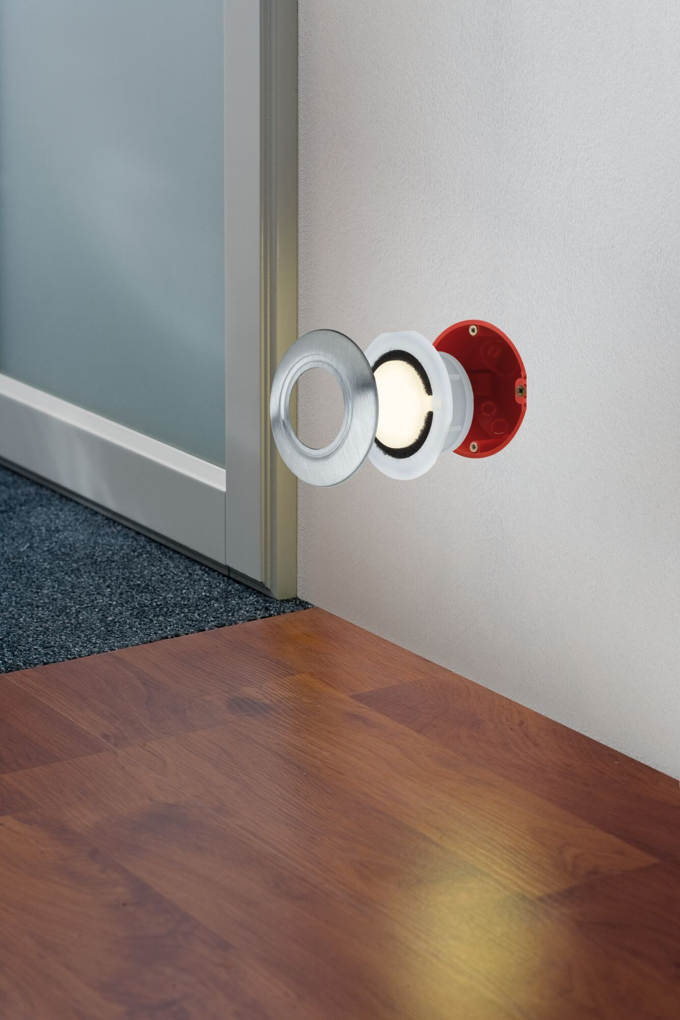Ein Wandlicht mit silbernem Ring und rotem Gehäuse leuchtet.
