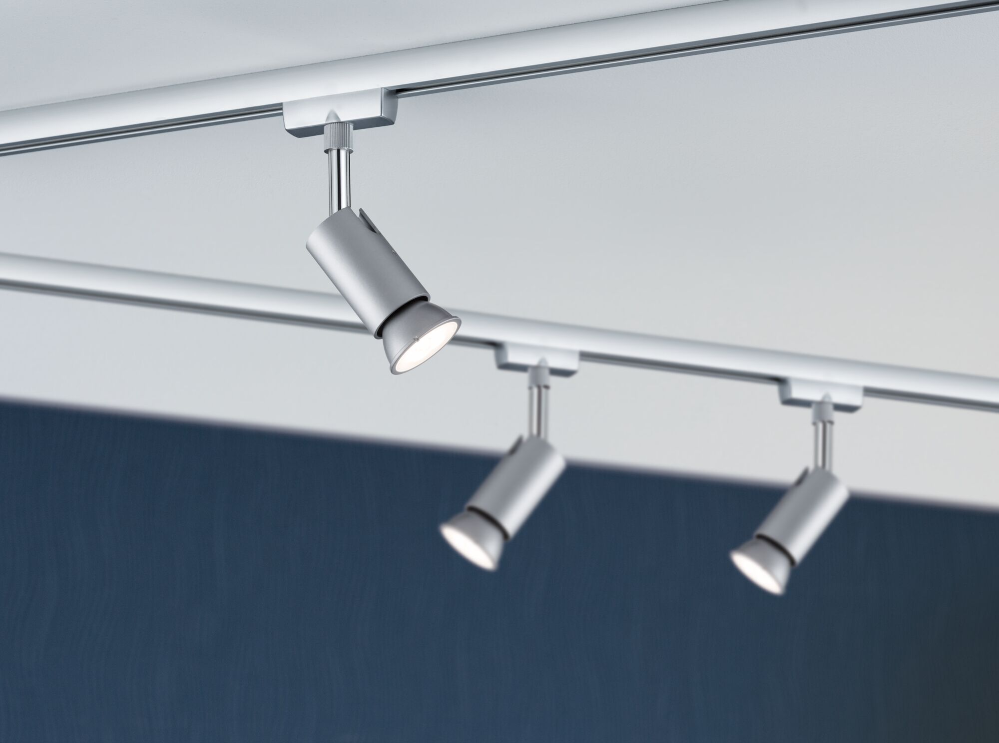 Tre faretti argentati sono montati su una guida a soffitto.
