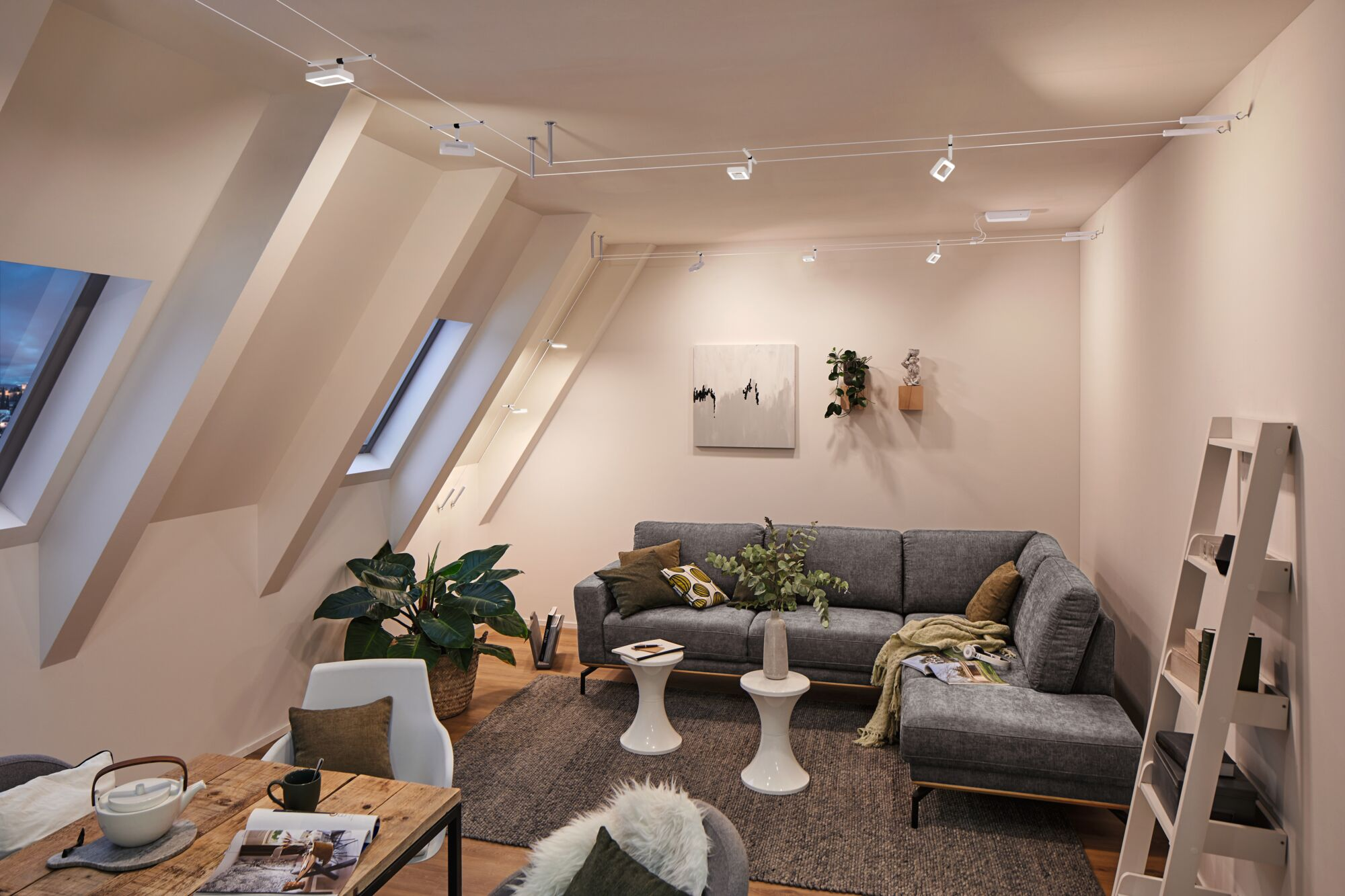 Ein gemütliches Wohnzimmer mit Dachschrägen, grauem Sofa und Holztisch.
