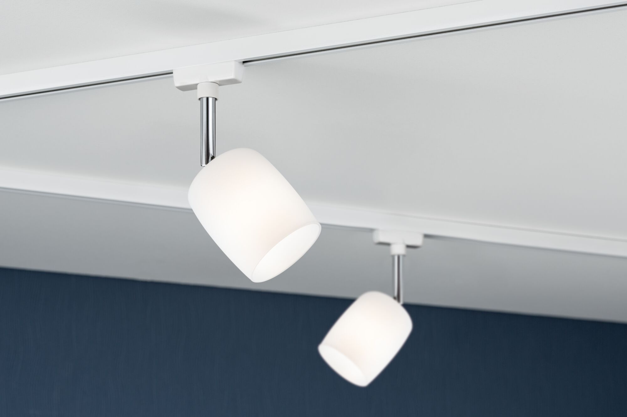 Due faretti da soffitto bianchi pendono da un binario bianco sopra un muro blu scuro.