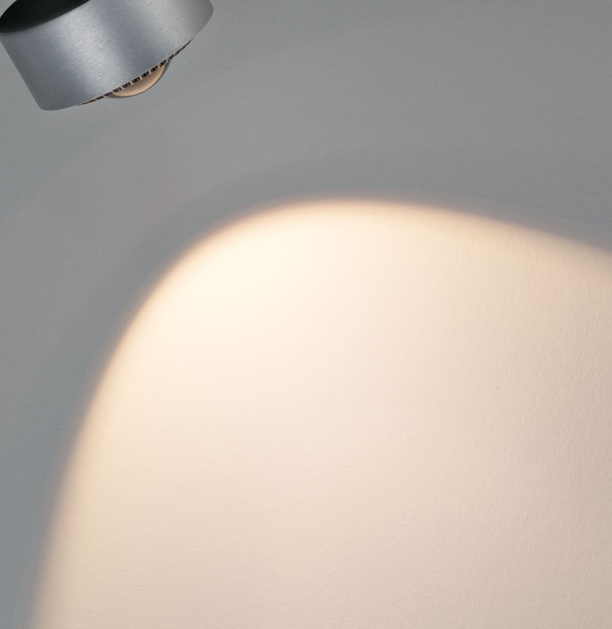 Un faretto argentato proietta un fascio di luce su un muro bianco.