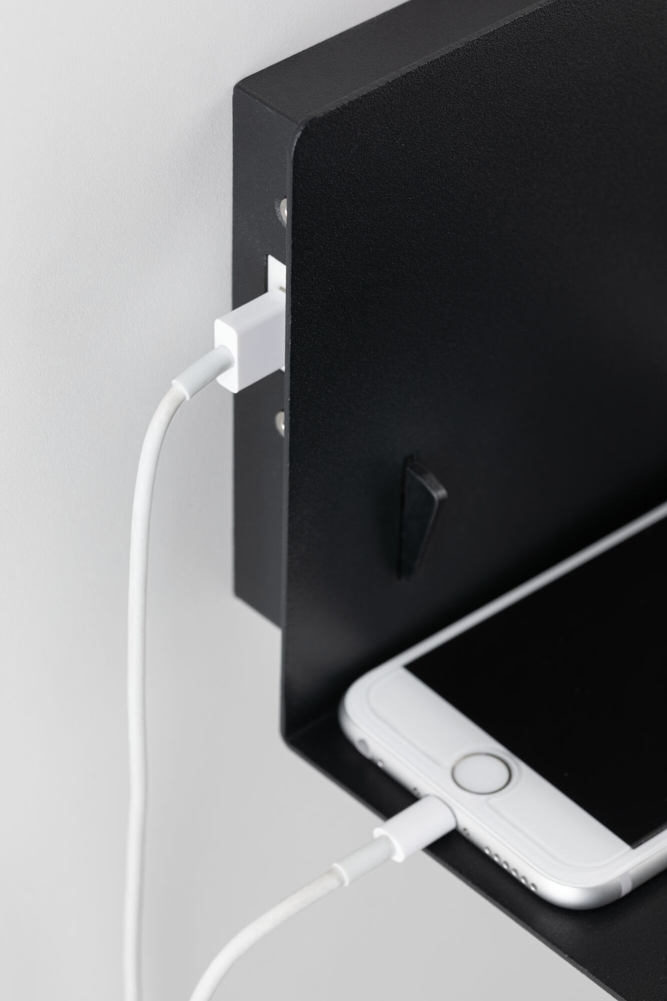 Ein weißes Smartphone wird an ein schwarzes Regal angeschlossen.