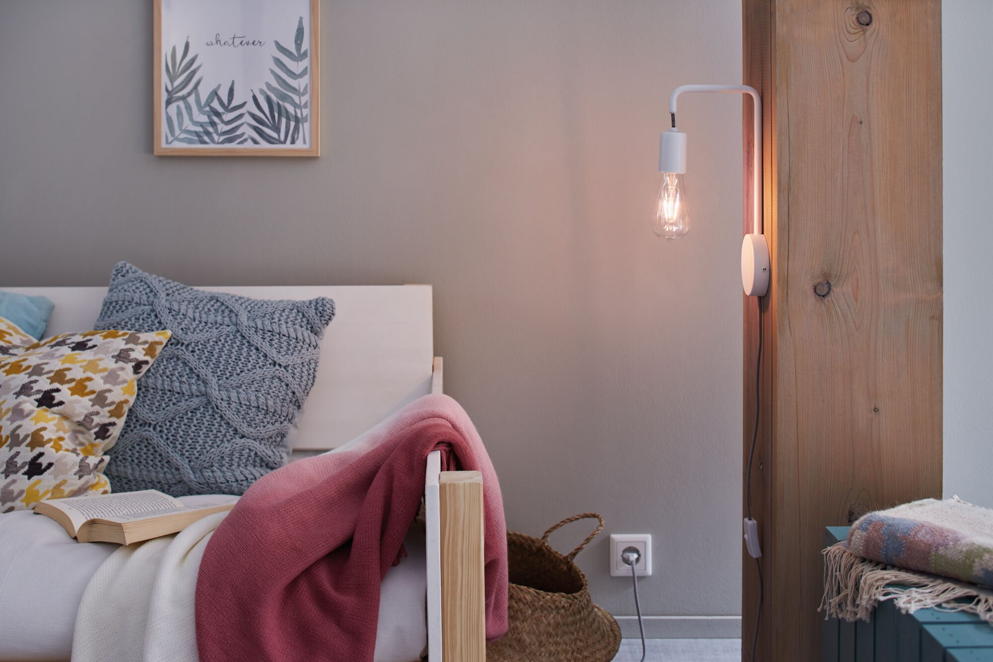 Łóżko z poduszkami, kocem, książką, lampą i koszykiem.