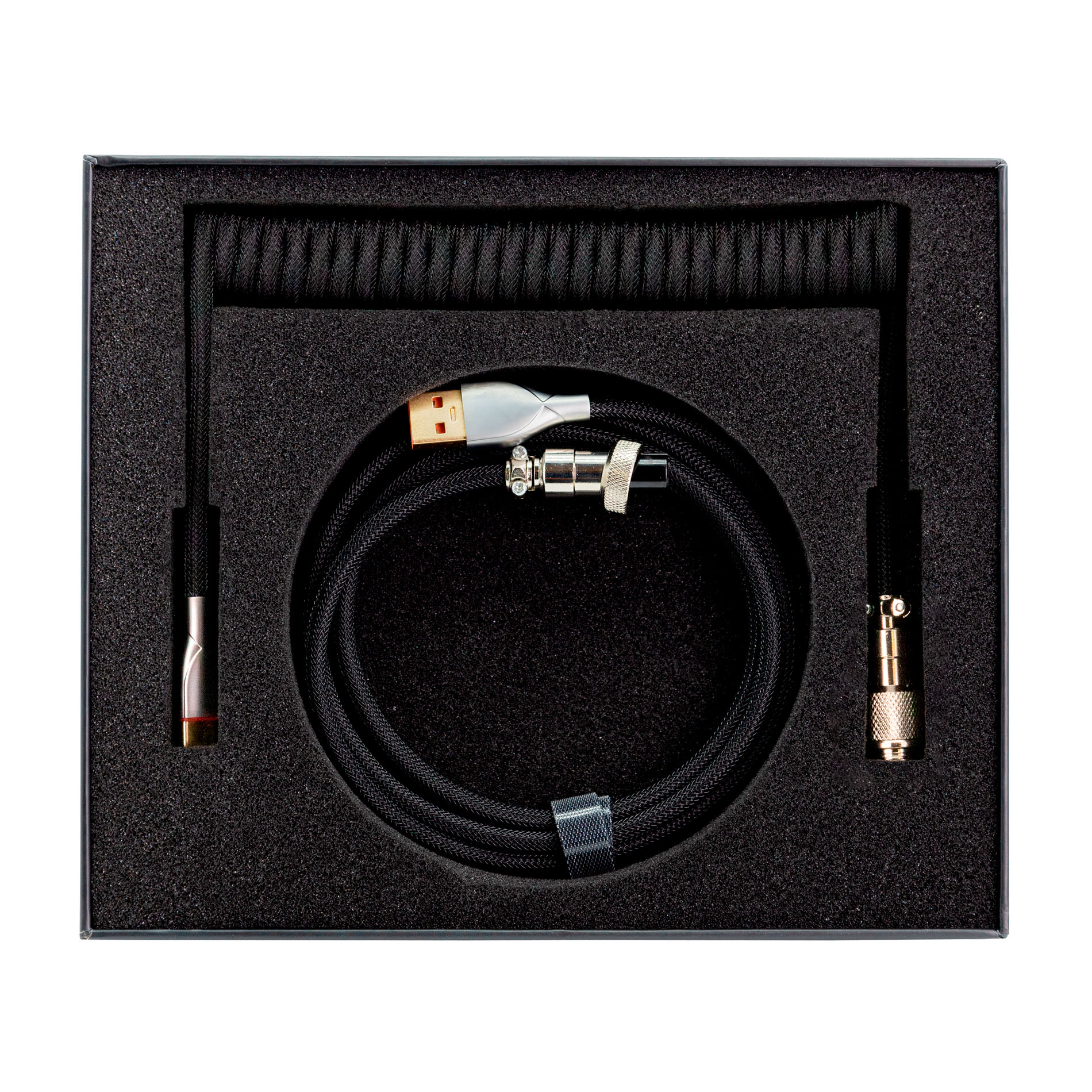Cable USB negro con secciones enrolladas y rectas en caja de espuma negra.