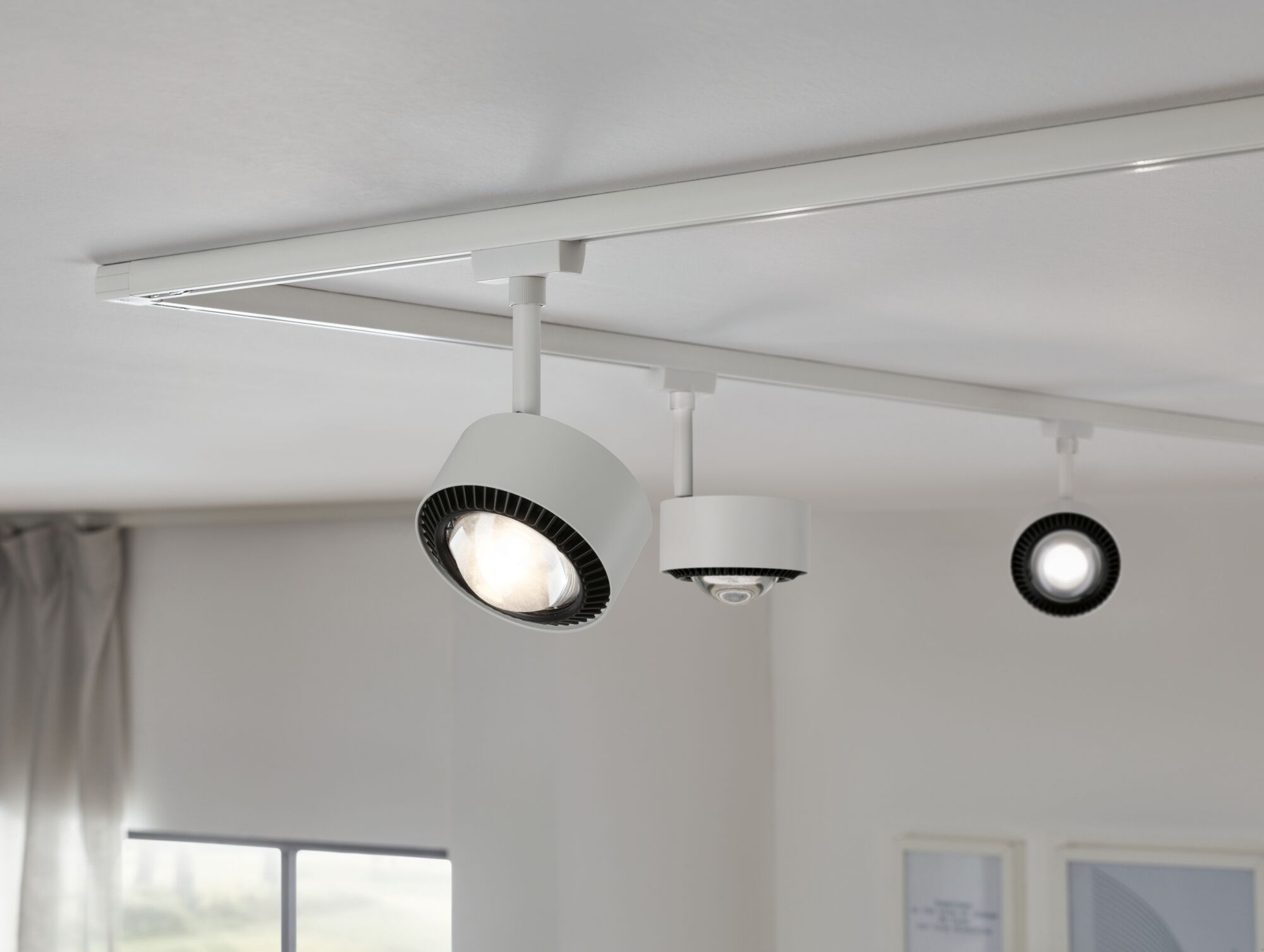 Weiße Schienenleuchten mit drei Lampen an einer weißen Decke.