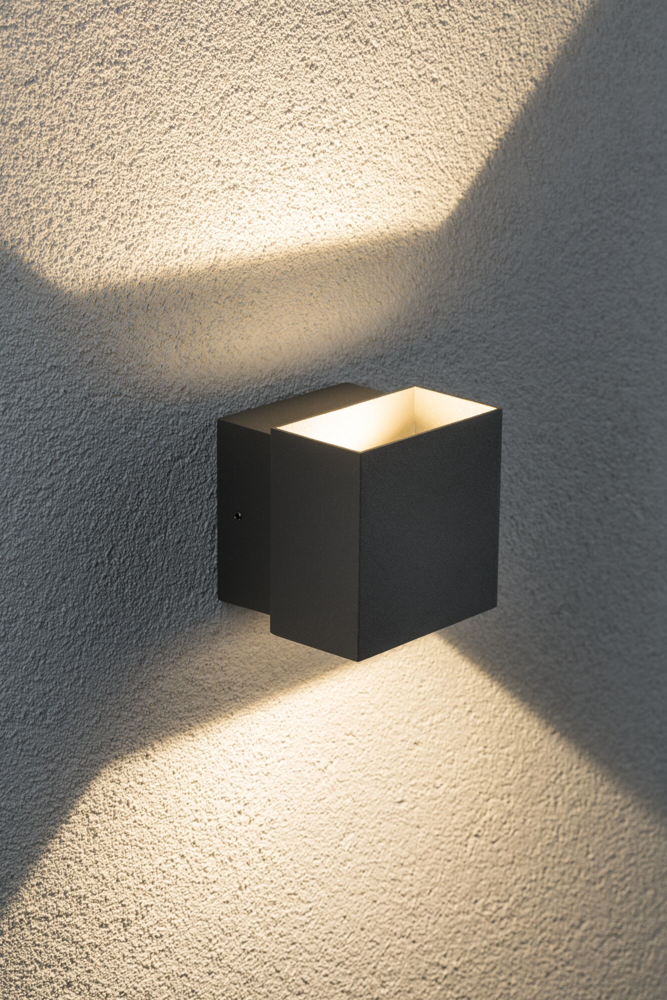 Czarna kostka kinkietowa oświetla teksturowaną ścianę plamami światła.