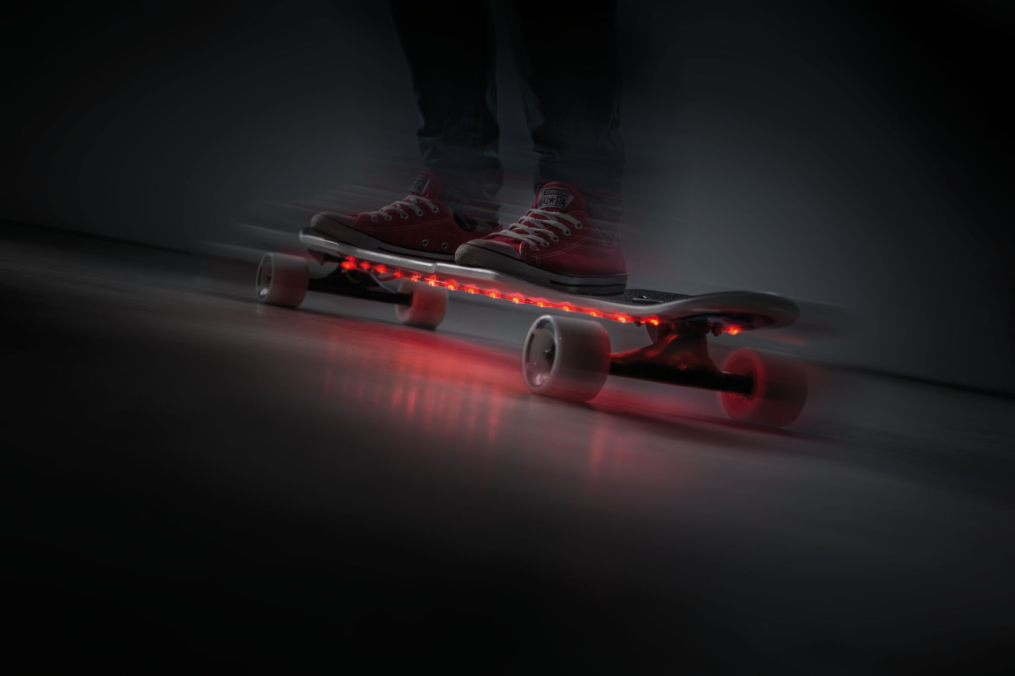 Person fährt Skateboard mit roten Lichtern, verschwommener Hintergrund.