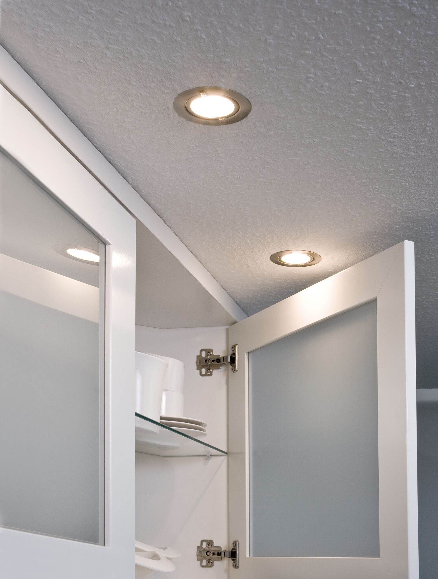 Einbauleuchten beleuchten eine weiße Decke über offenen weißen Schränken mit Glasböden.