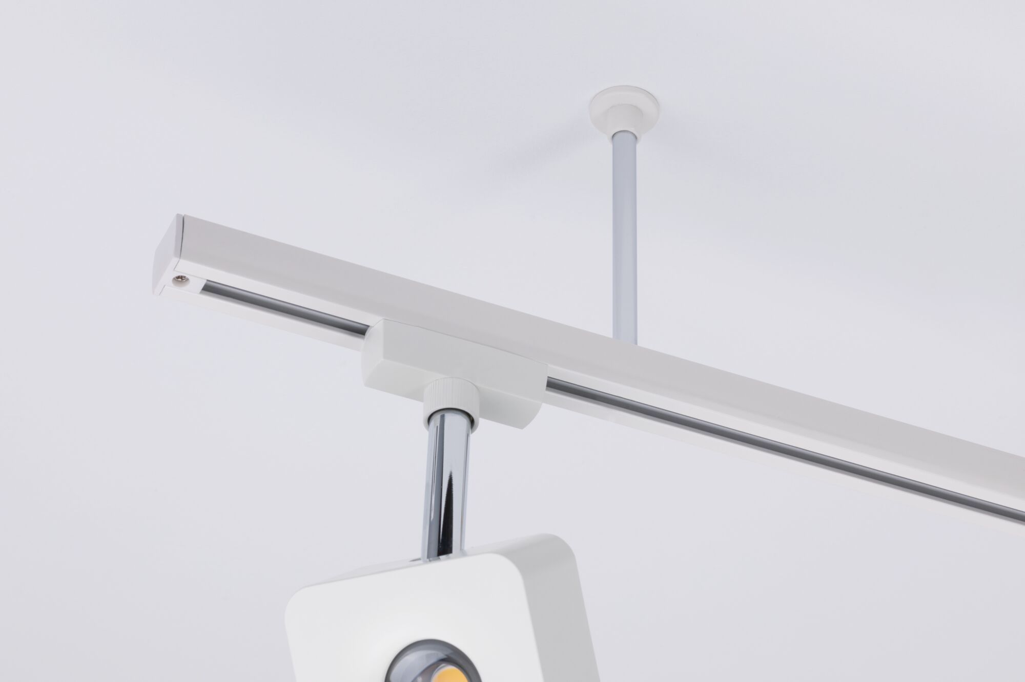 Ein weißer Deckenstrahler mit verchromtem Arm auf einer weißen Decke.