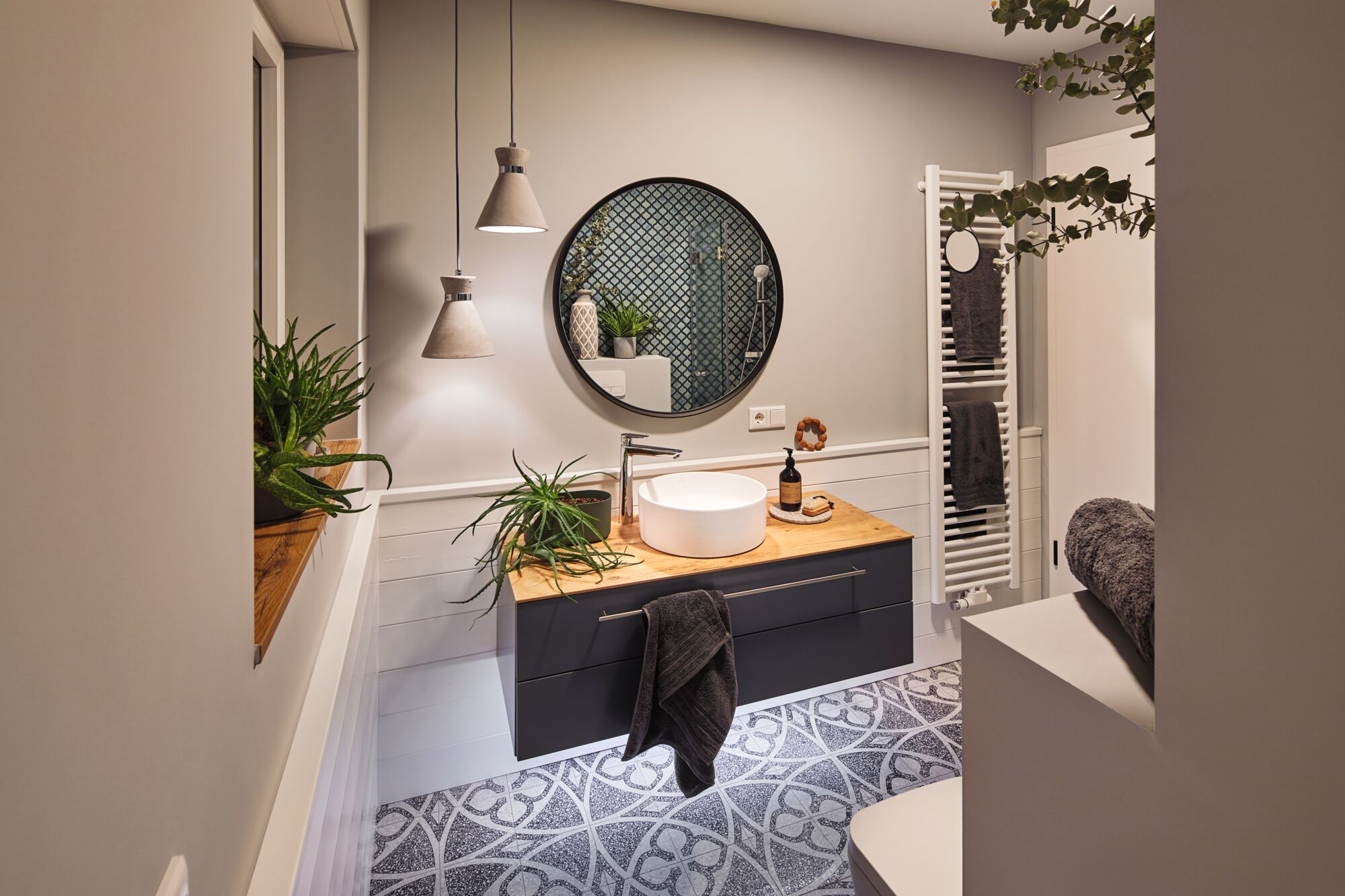 Modernes Badezimmer mit Waschbecken, Spiegel, Handtuchwärmer und Pflanzen.