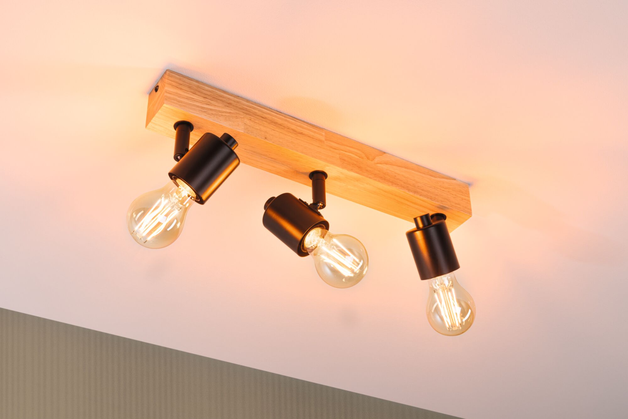 Lampa sufitowa z drewnianą podstawą i trzema czarnymi oprawkami z żarówkami.