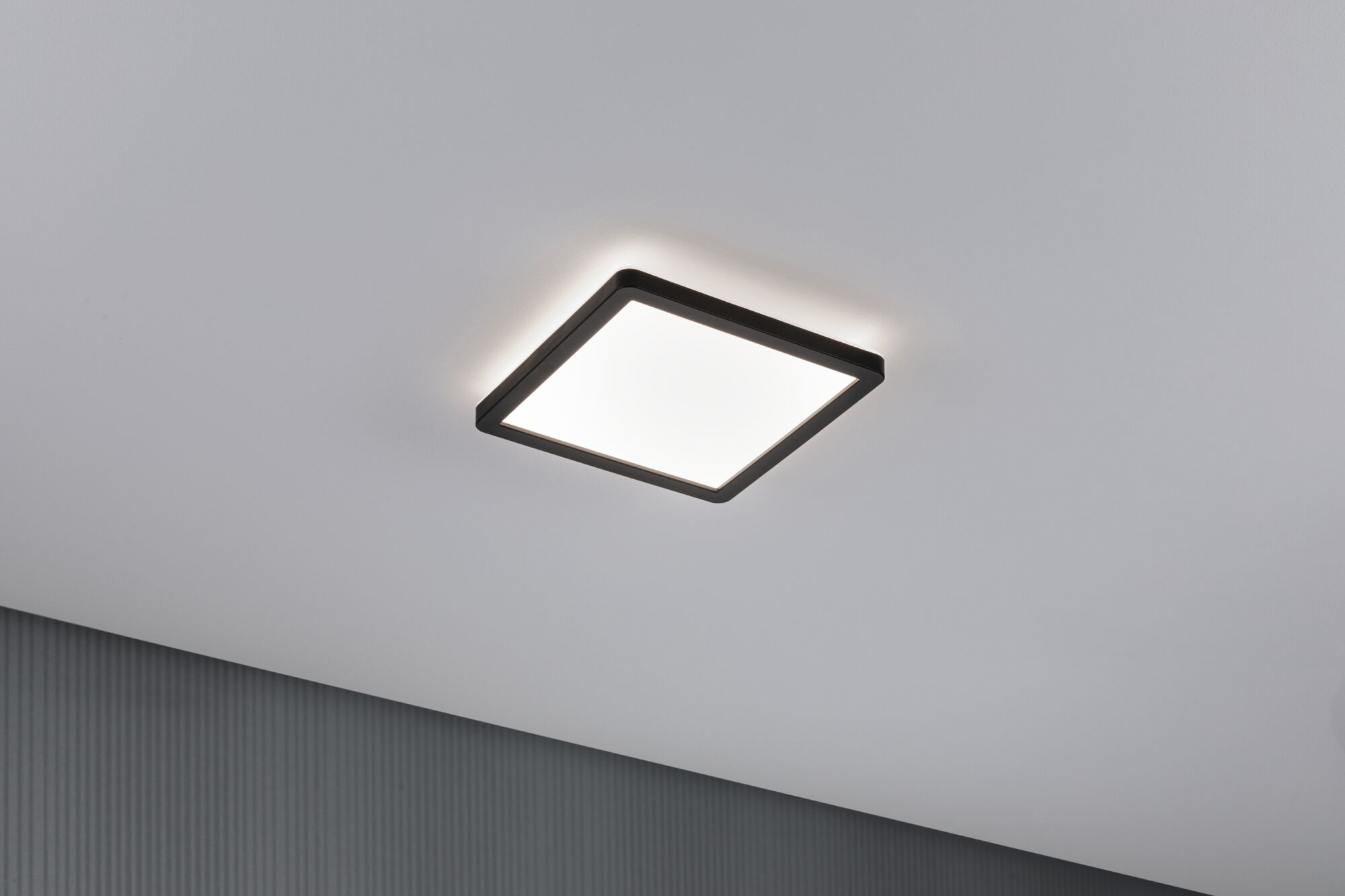 Una plafoniera quadrata con cornice nera illumina un soffitto bianco.