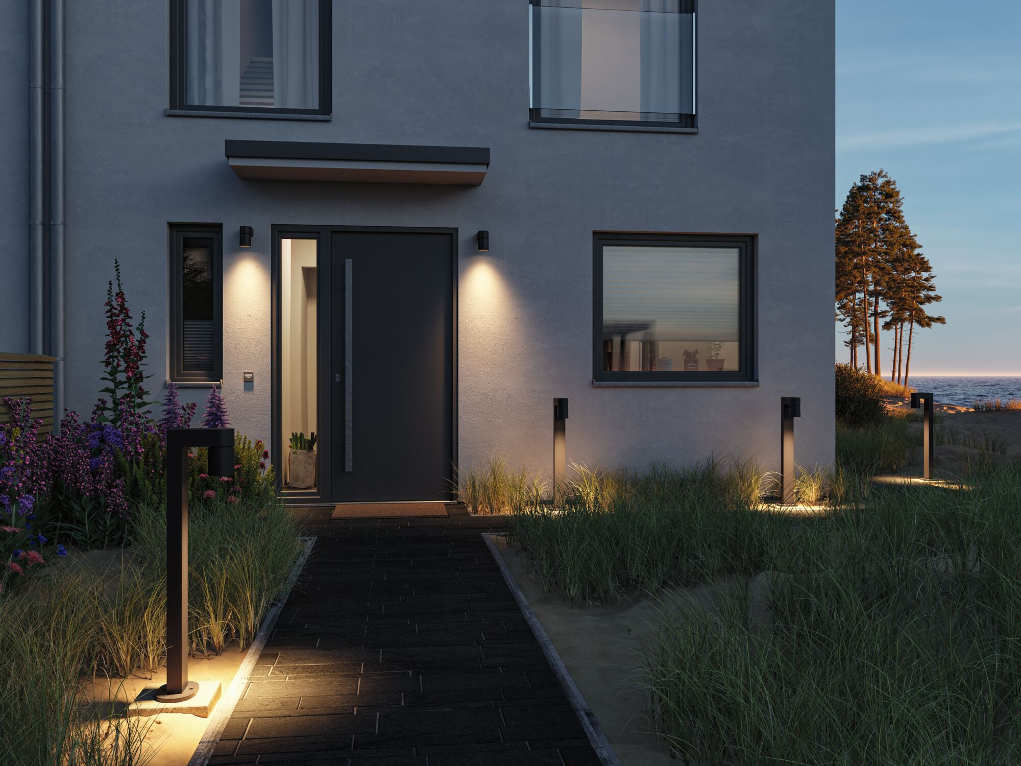 Nowoczesny dom z ciemnymi drzwiami, oświetloną ścieżką i morzem w tle.