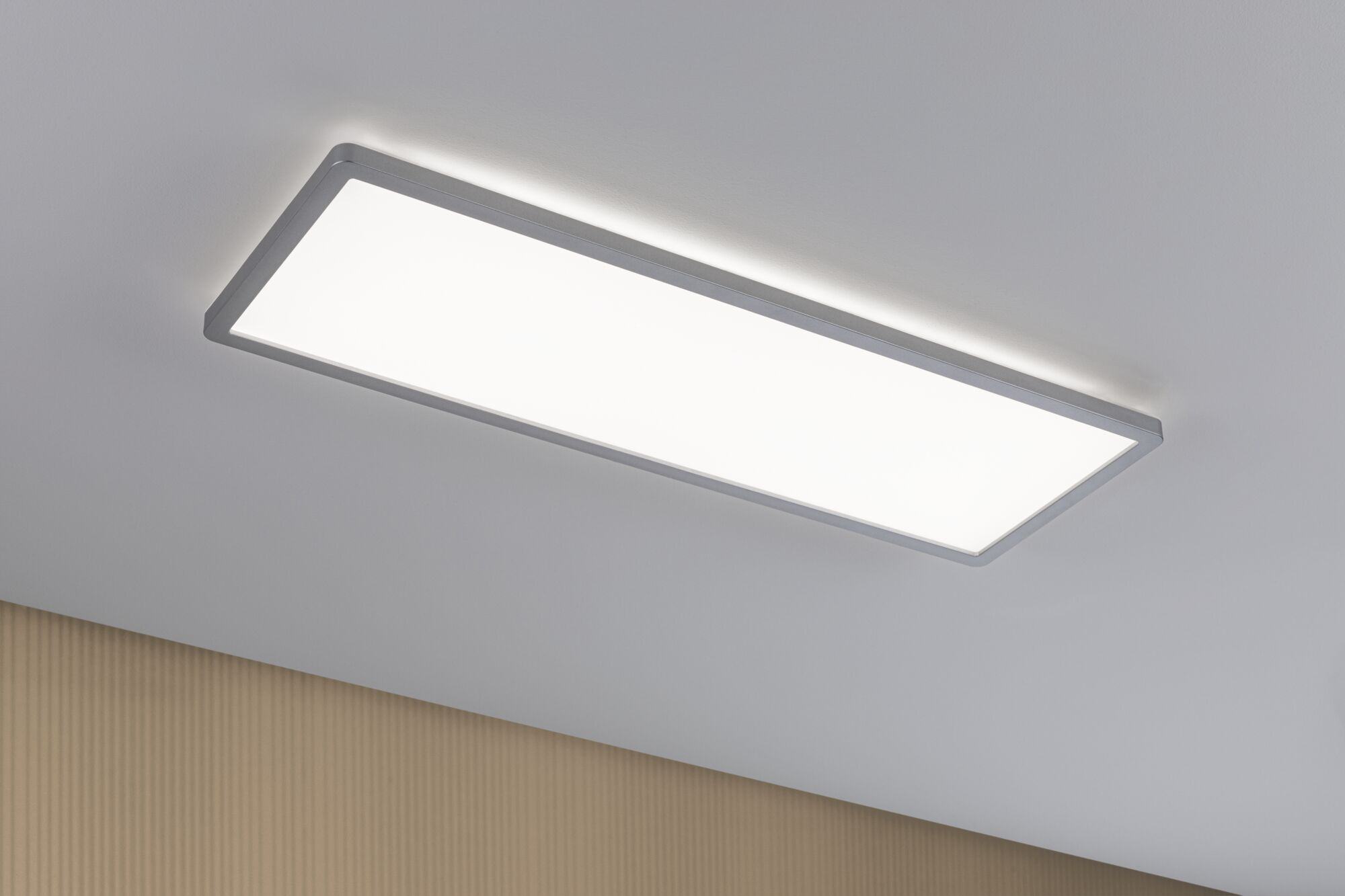 Prostokątna lampa sufitowa z srebrną ramą jasno świeci na białym suficie.