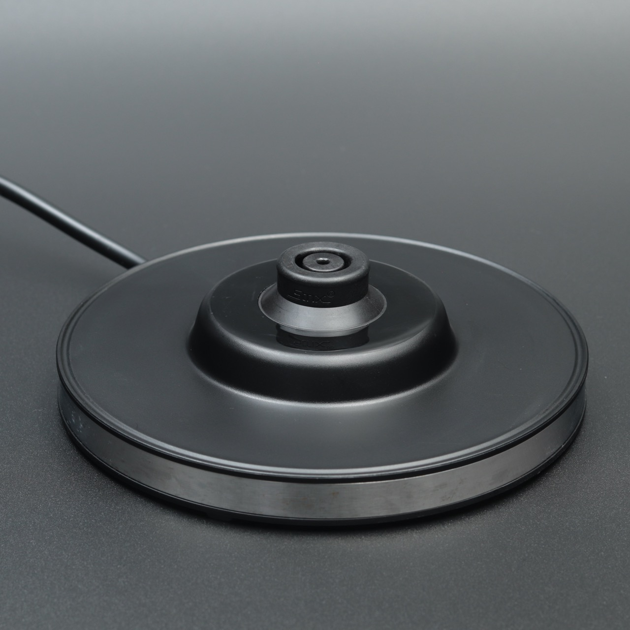 Schwarzer Wasserkocherfuß mit silbernem Ring und Kabel auf dunklem Hintergrund.