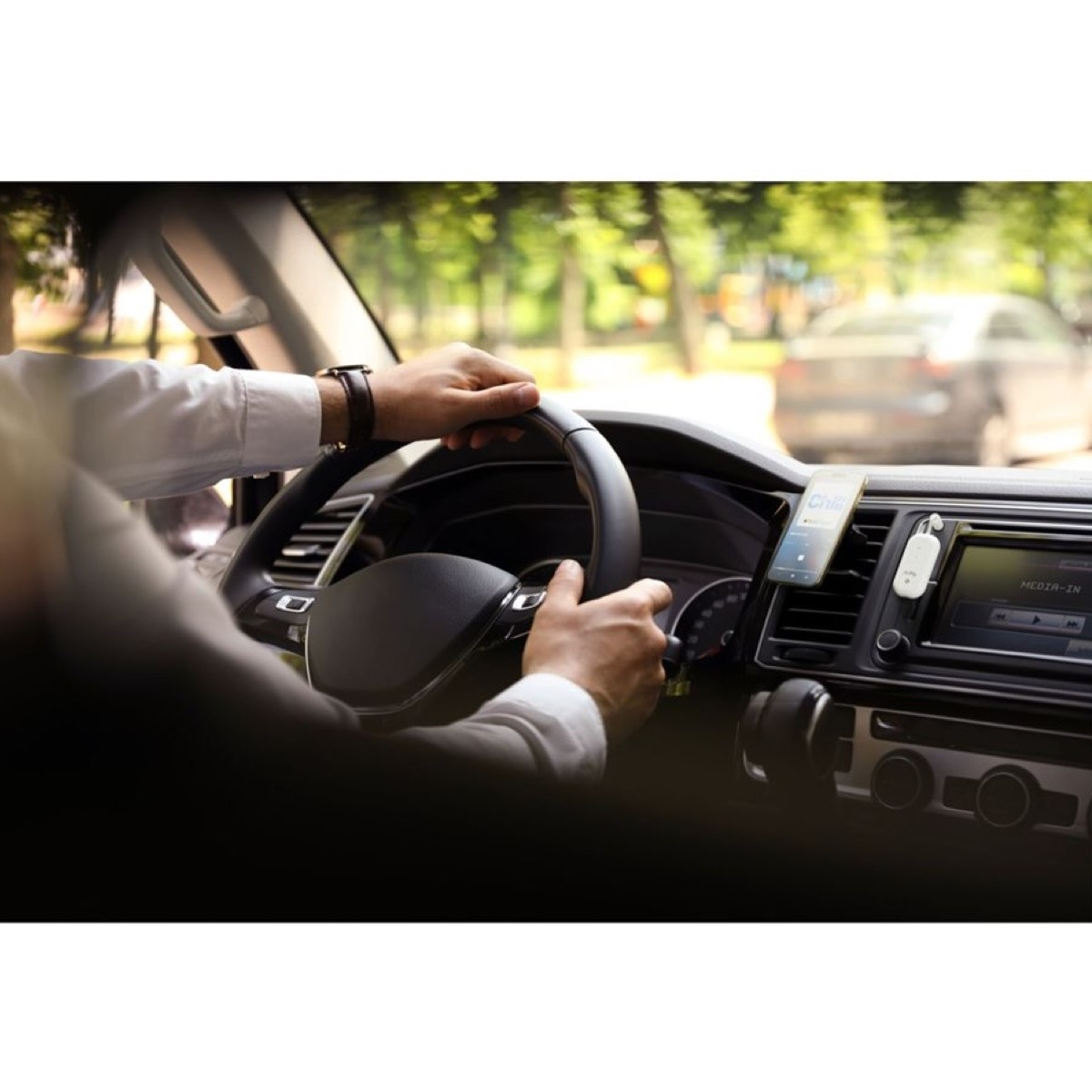 Uomo guida auto, mani sul volante, telefono su bocchetta aria.