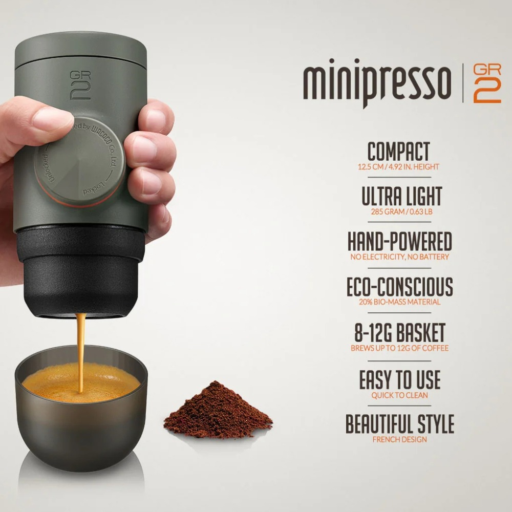 Handgehaltener Kaffeeproduzent presst Espresso in eine Tasse. Kaffeepulver liegt daneben.