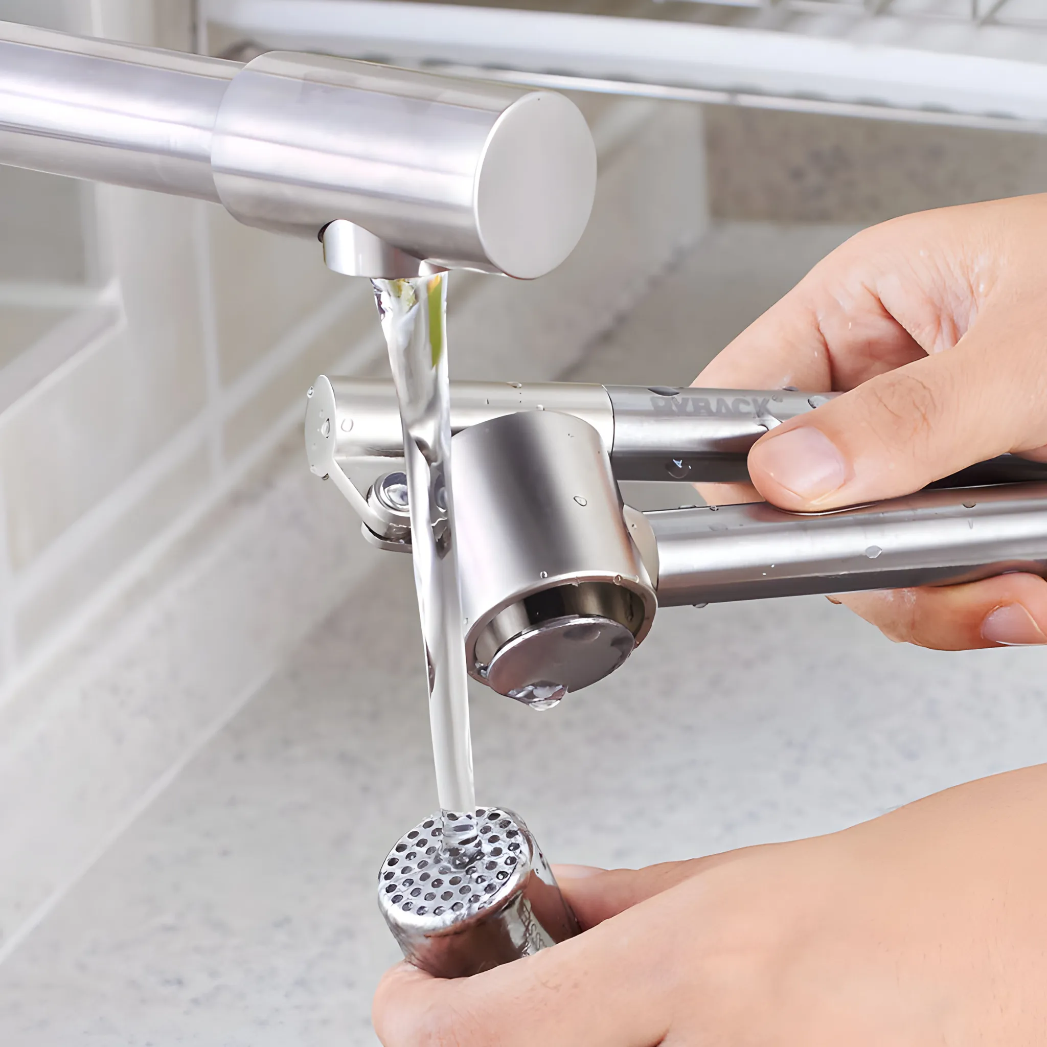 Eine Hand hält eine silberne Knoblauchpresse unter fließendes Wasser.