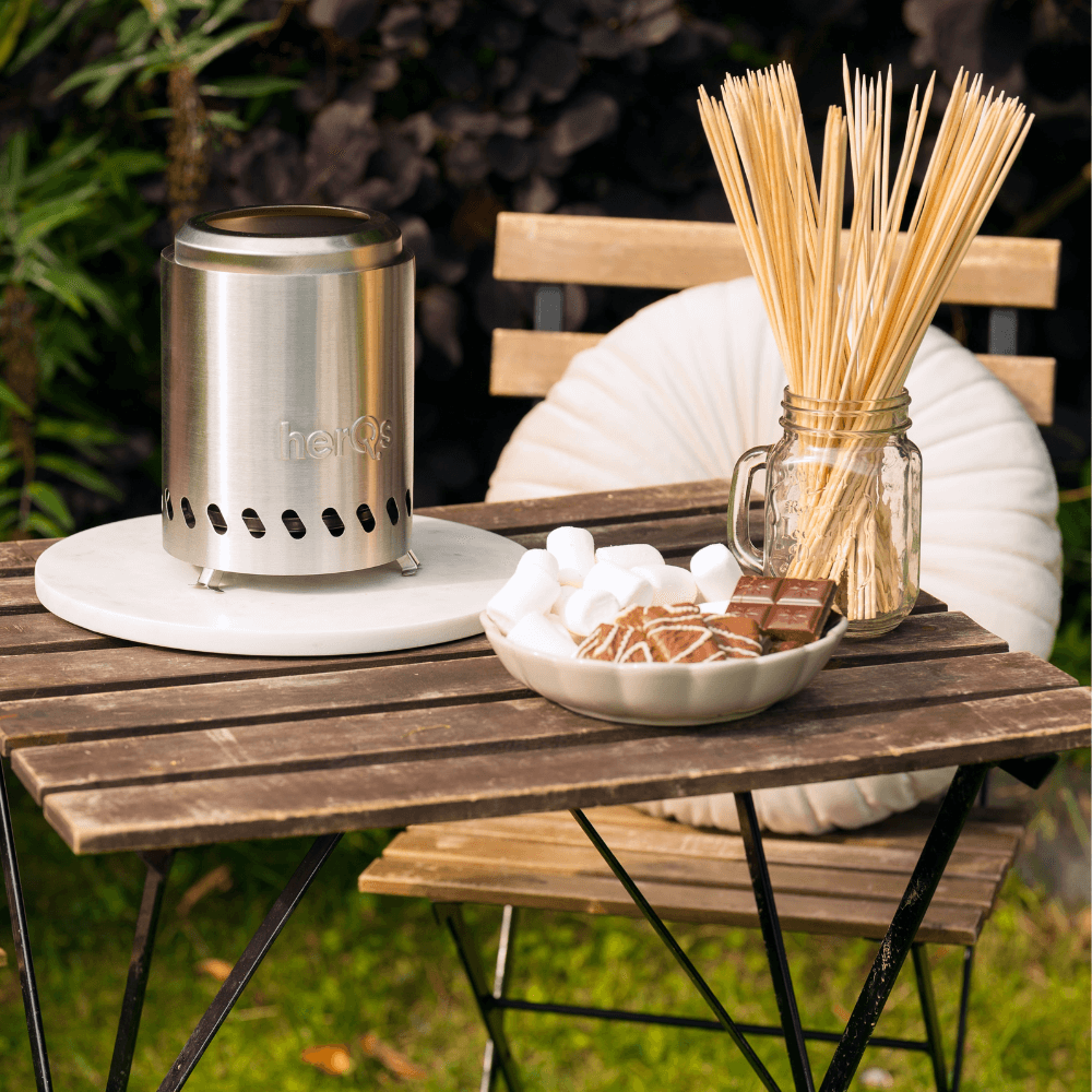 Ein tragbarer Kamin mit Marshmallows, Schokolade und Spießen auf einem Holztisch.