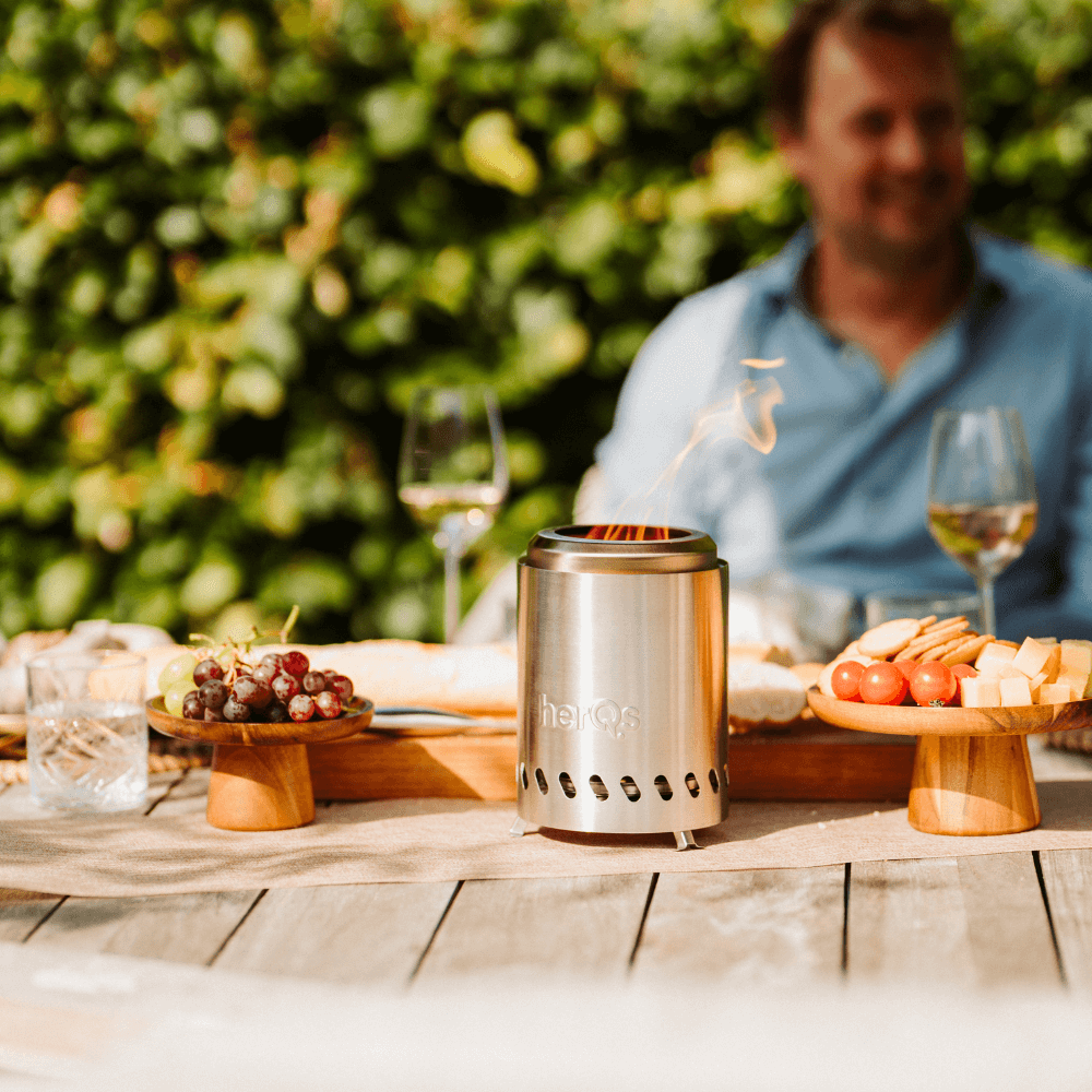 Ein Mann sitzt an einem Tisch mit einem kleinen Ofen, Wein und Essen im Freien.