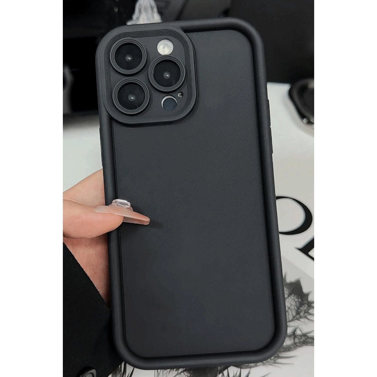 Üç kamera lensi ve flaşlı siyah telefon kılıfı, bir el tarafından tutuluyor.