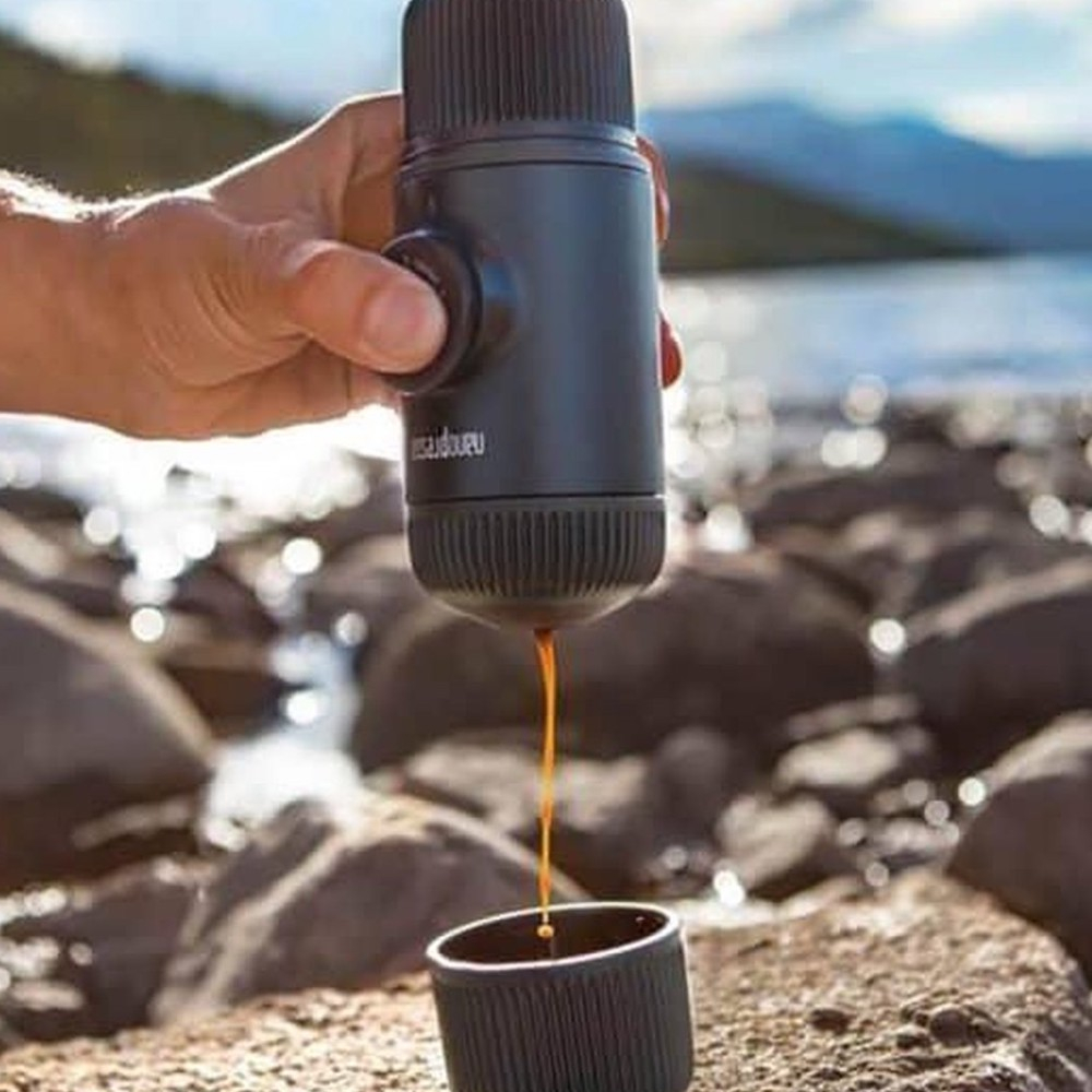 Eine Hand hält eine Kaffeemaschine, die Kaffee in eine kleine Tasse gießt.