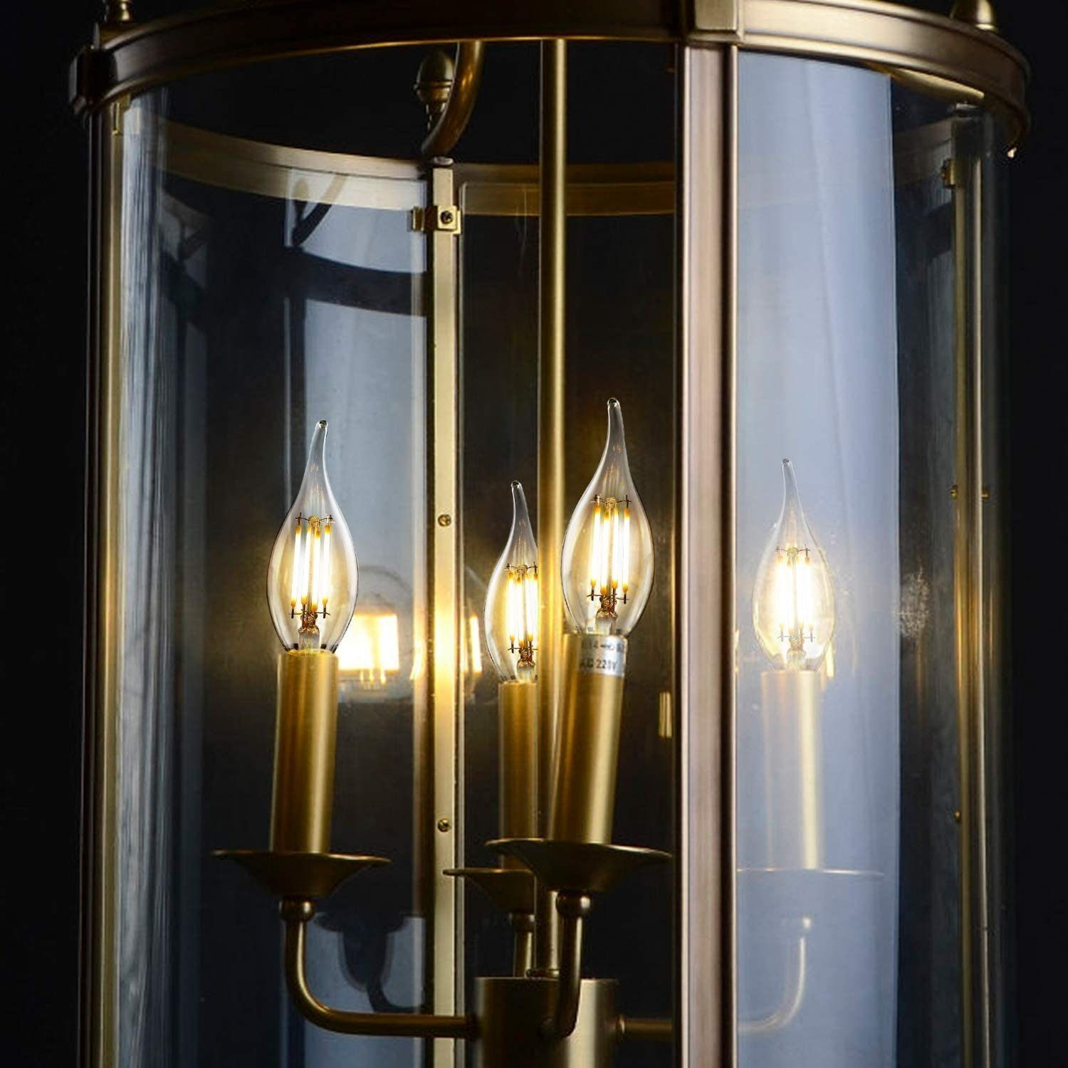 Lanterna in ottone con quattro lampadine a candela e paralumi in vetro su sfondo scuro.