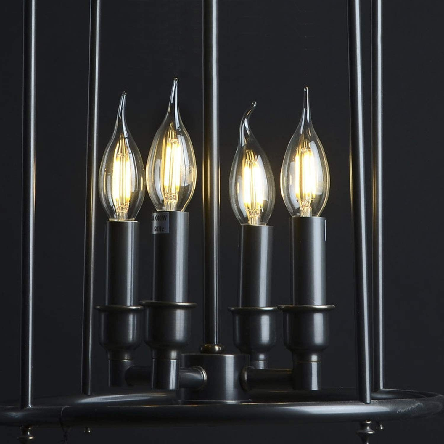 Quattro lampadine a forma di fiamma in un lampadario scuro a gabbia.