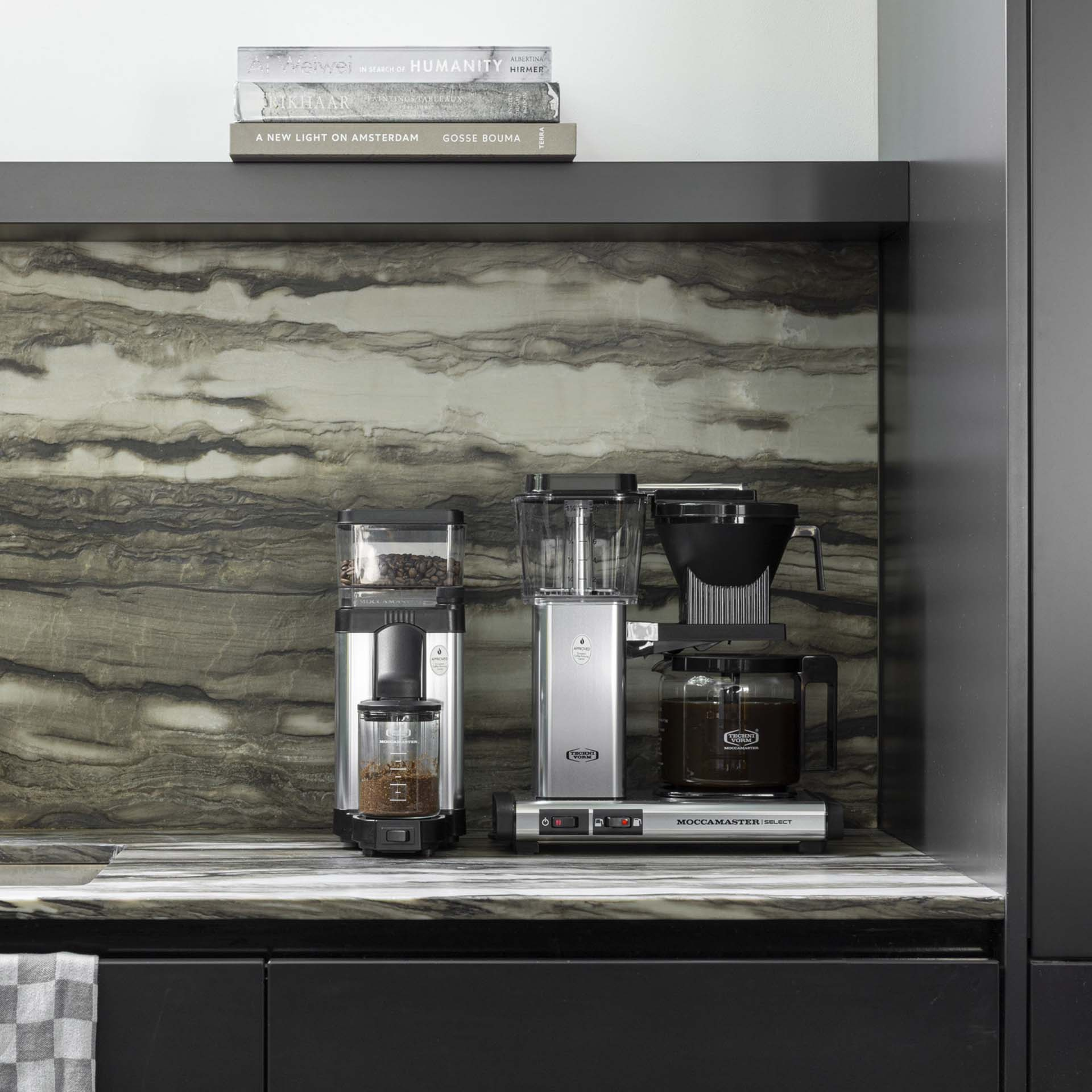 Two silver coffee makers sit on a marble counter in front of a patterned backsplash.