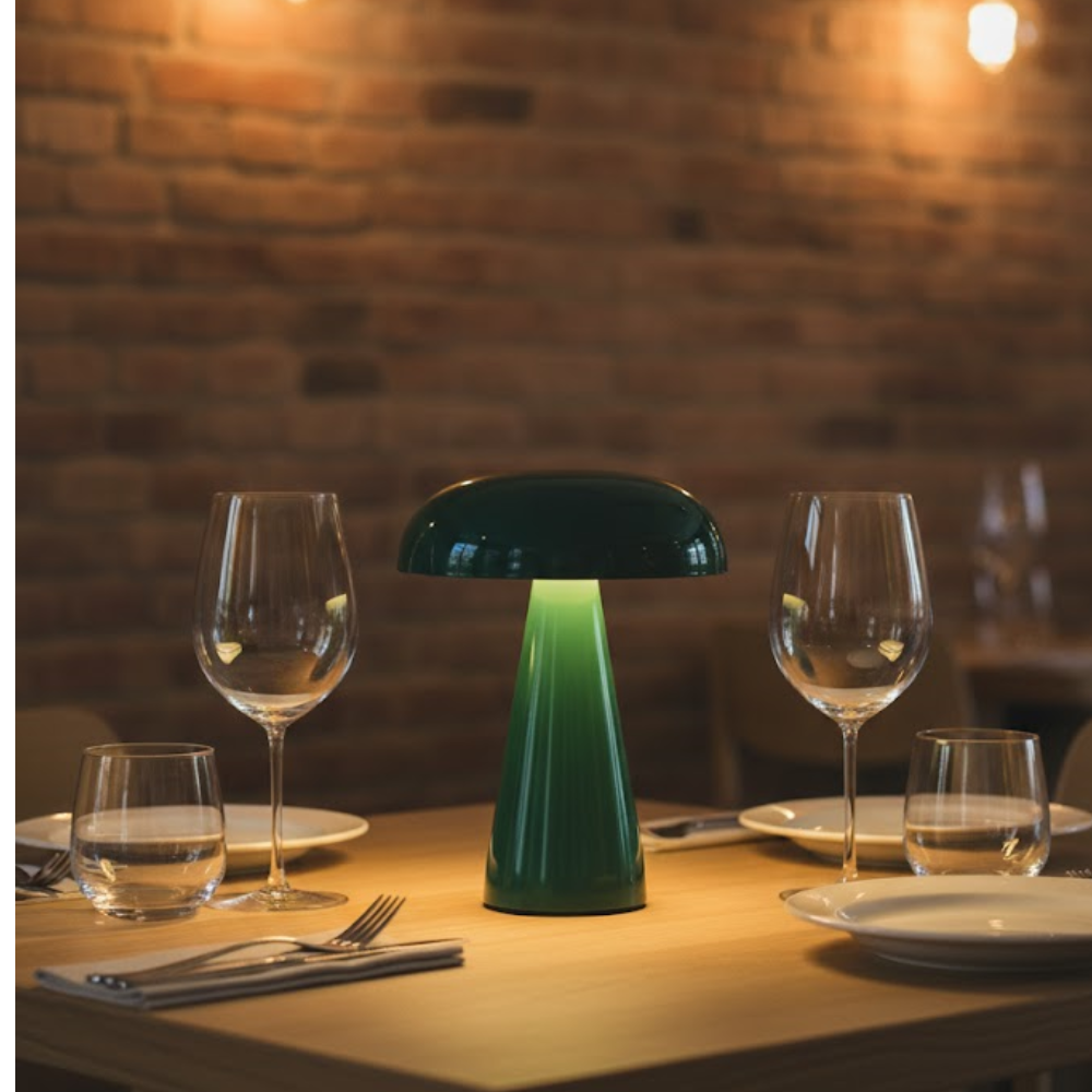 Groene paddenstoellamp op houten tafel met glazen en borden, bakstenen muur achtergrond.