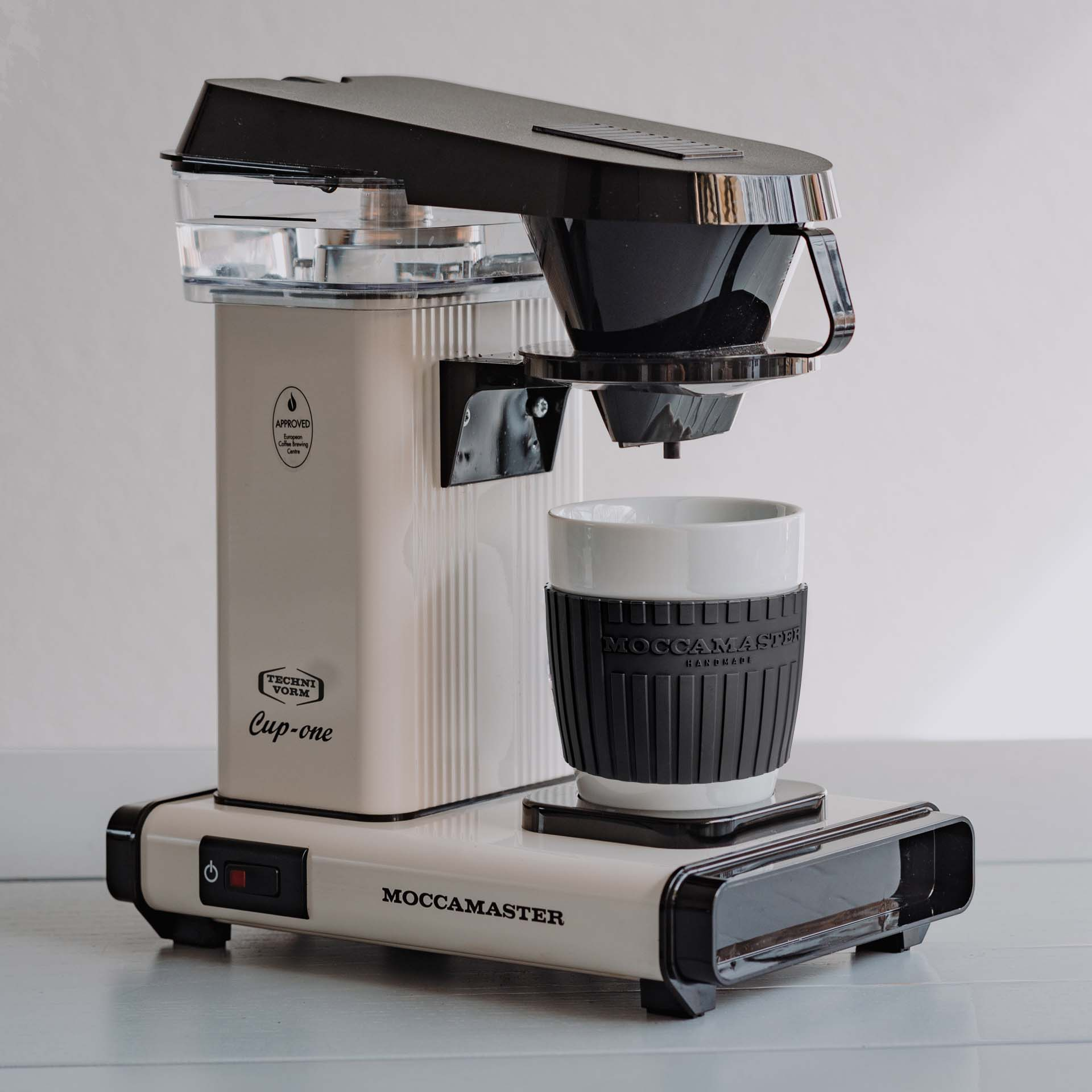 Eine weiße Kaffeemaschine mit schwarzem Filterhalter und weißer Tasse mit schwarzem Griff.