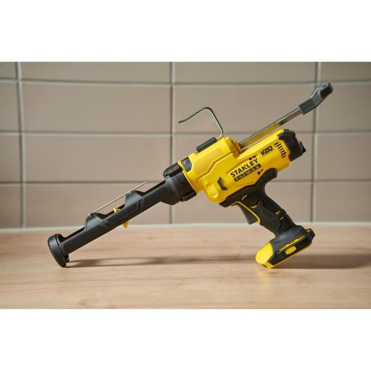 Pistola per silicone a batteria gialla e nera su tavolo di legno, muro piastrellato.