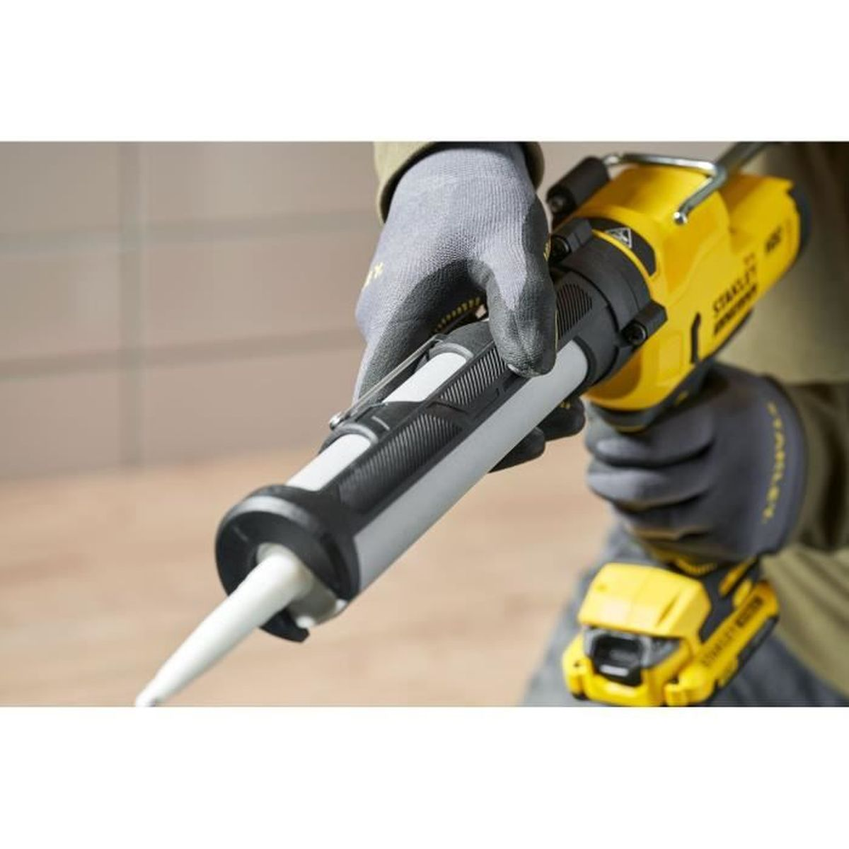 Persona con guanti opera pistola per silicone a batteria gialla con tubo grigio.