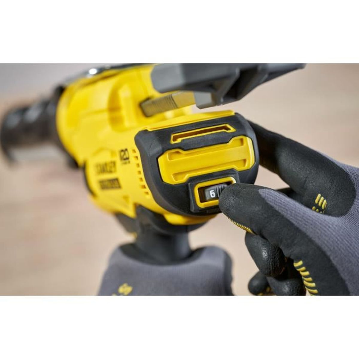 Una mano con guanto grigio regola il numero 6 su un elettroutensile giallo.