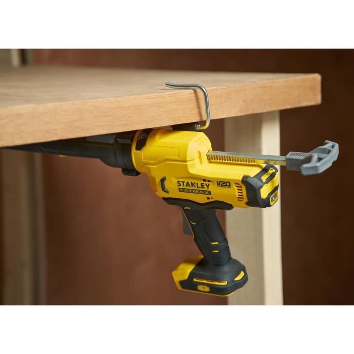 Pistola per silicone a batteria gialla fissata a una superficie in legno.