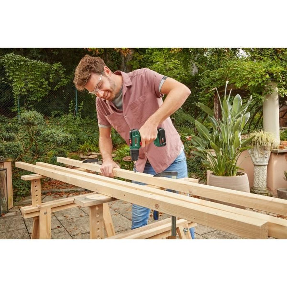 Ein Mann bohrt Holzbretter in einem Garten.