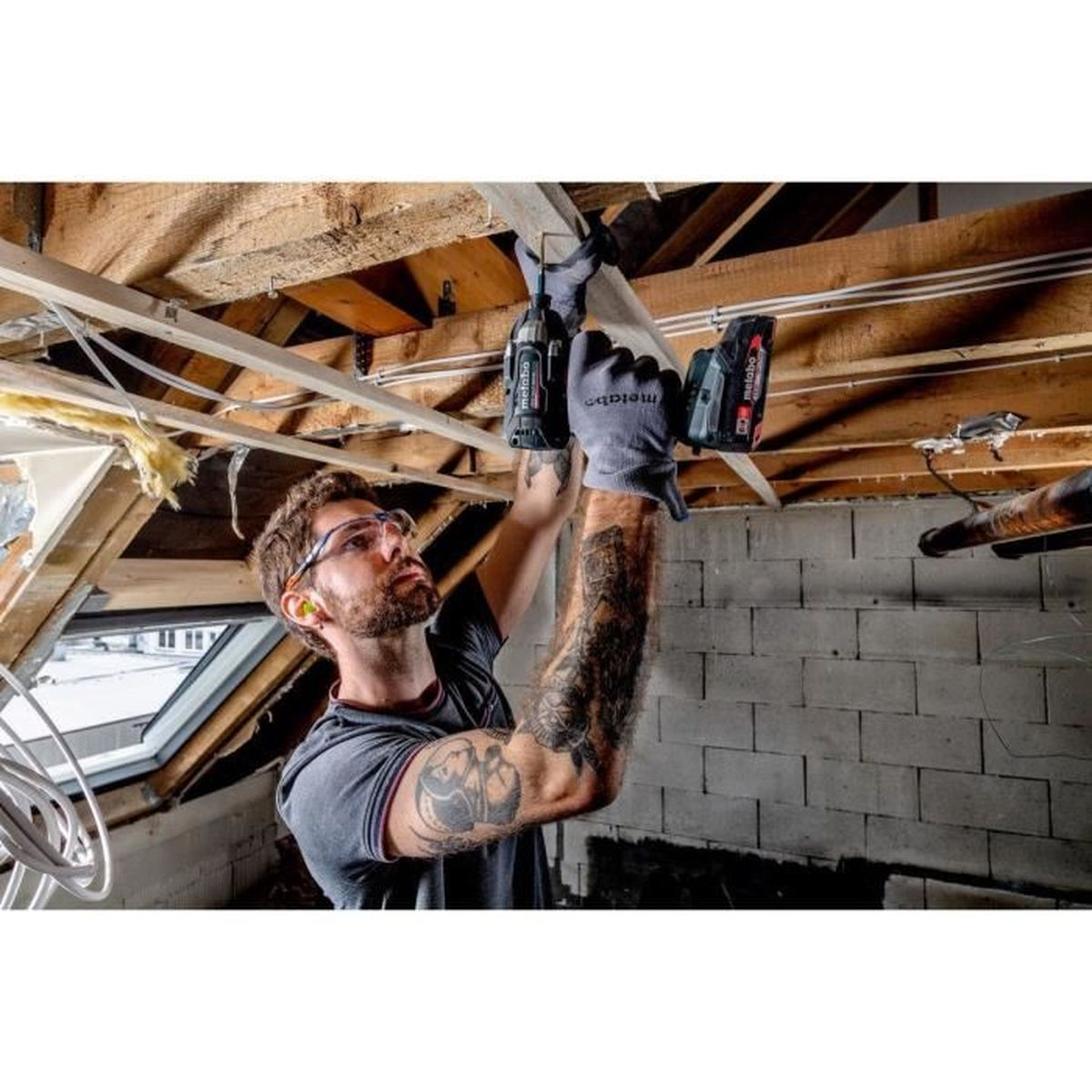 Ein Mann mit Brille und Handschuhen bohrt in eine Decke aus Holz.