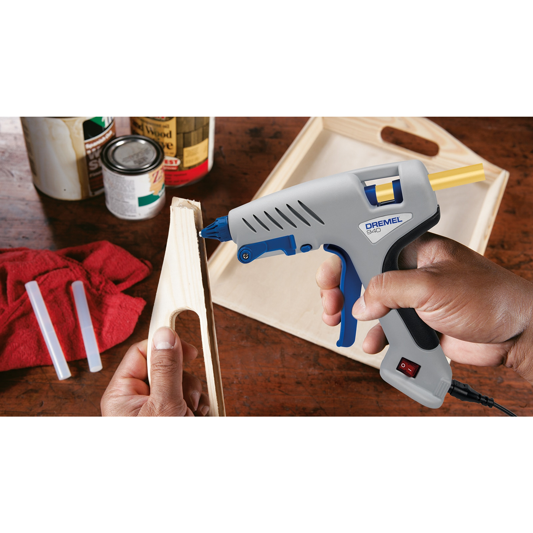 Eine Hand hält eine Heißklebepistole, die Klebstoff auf Holz aufträgt.
