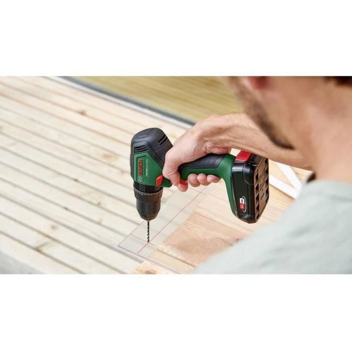 Mann bohrt Holz mit grüner Bosch Bohrmaschine, klare Schablone auf Holz.