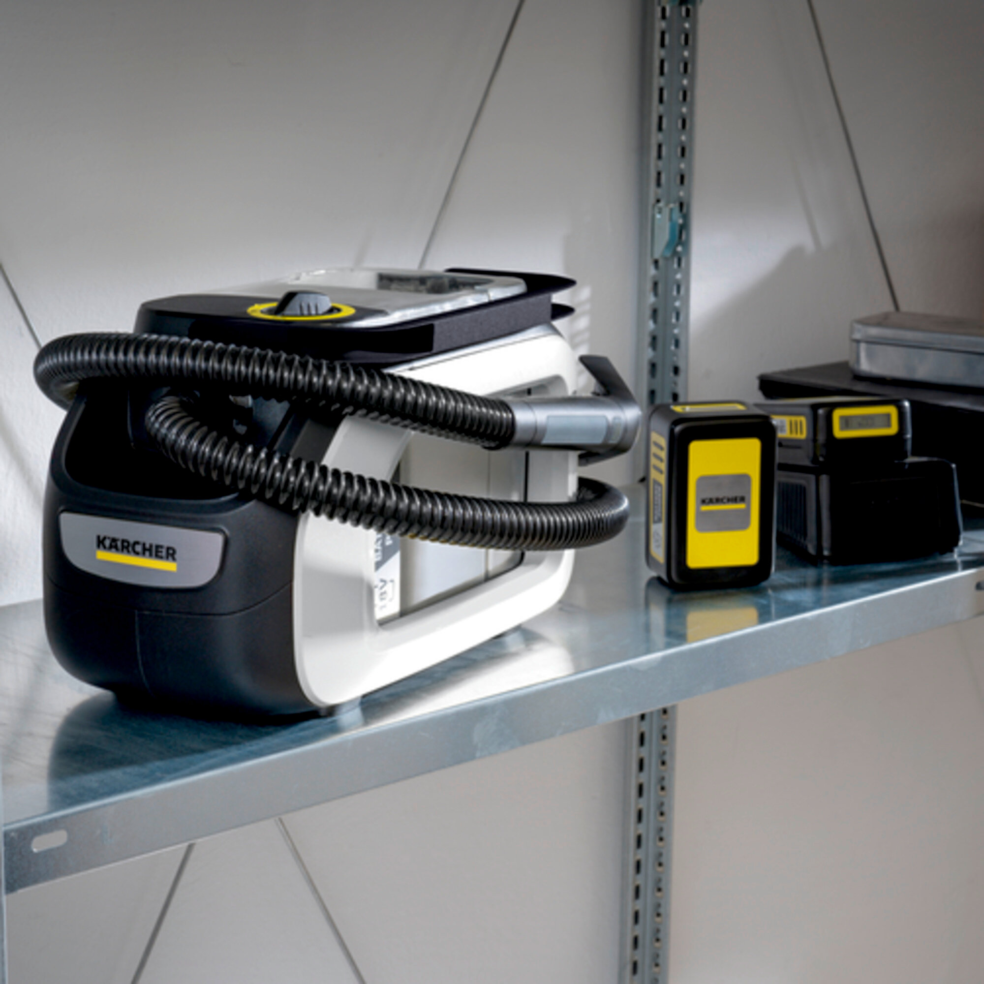 Odkurzacz Kärcher z wężem i dwoma akumulatorami na półce.